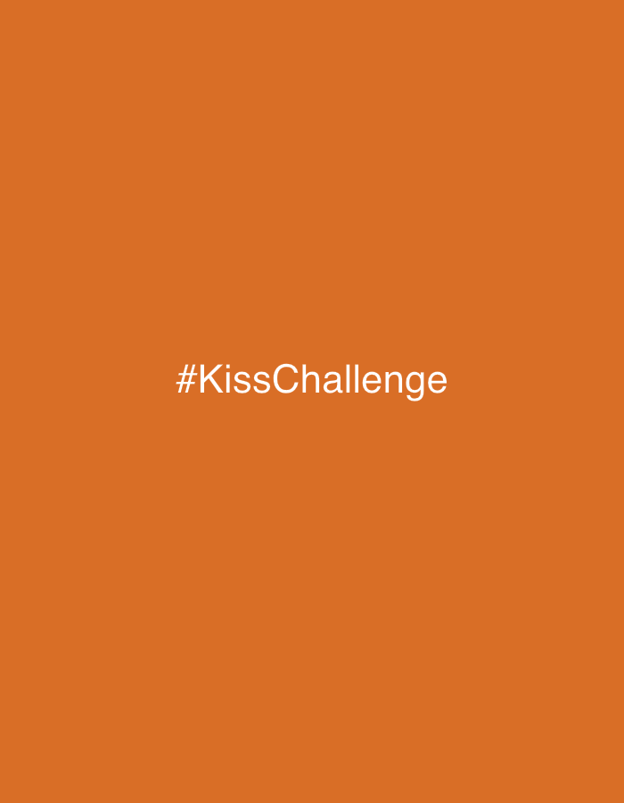 The image displays a solid, uniform orange background. Centered horizontally and vertically on this background is the white text "#KissChallenge". The text consists of a hashtag symbol followed by the words "Kiss" and "Challenge" concatenated, with "K" and "C" capitalized. There are no other visible subjects, objects, people, actions, or environmental elements. The image is a digital graphic and does not depict a physical location in Petah Tikva, Israel, or any other city.