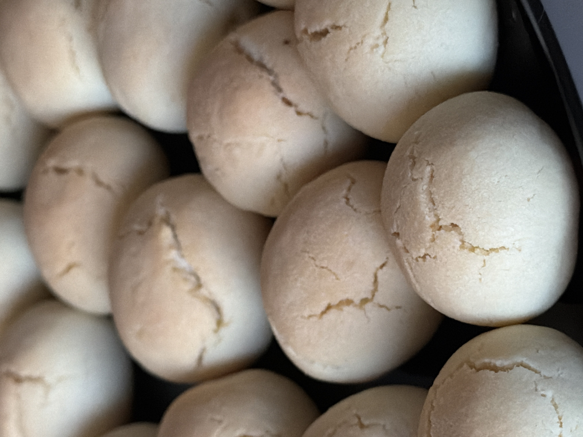 The image displays a close-up, overhead view of a batch of pale, round pastries arranged on a dark surface. The pastries appear to be slightly cracked on their surfaces and have a soft, matte texture. The lighting suggests an indoor setting, likely a kitchen or bakery. There is no visible indication of the city of Izhevsk, Russia, or any specific location. The scene focuses solely on the food item, with no people, actions, or interactions depicted.