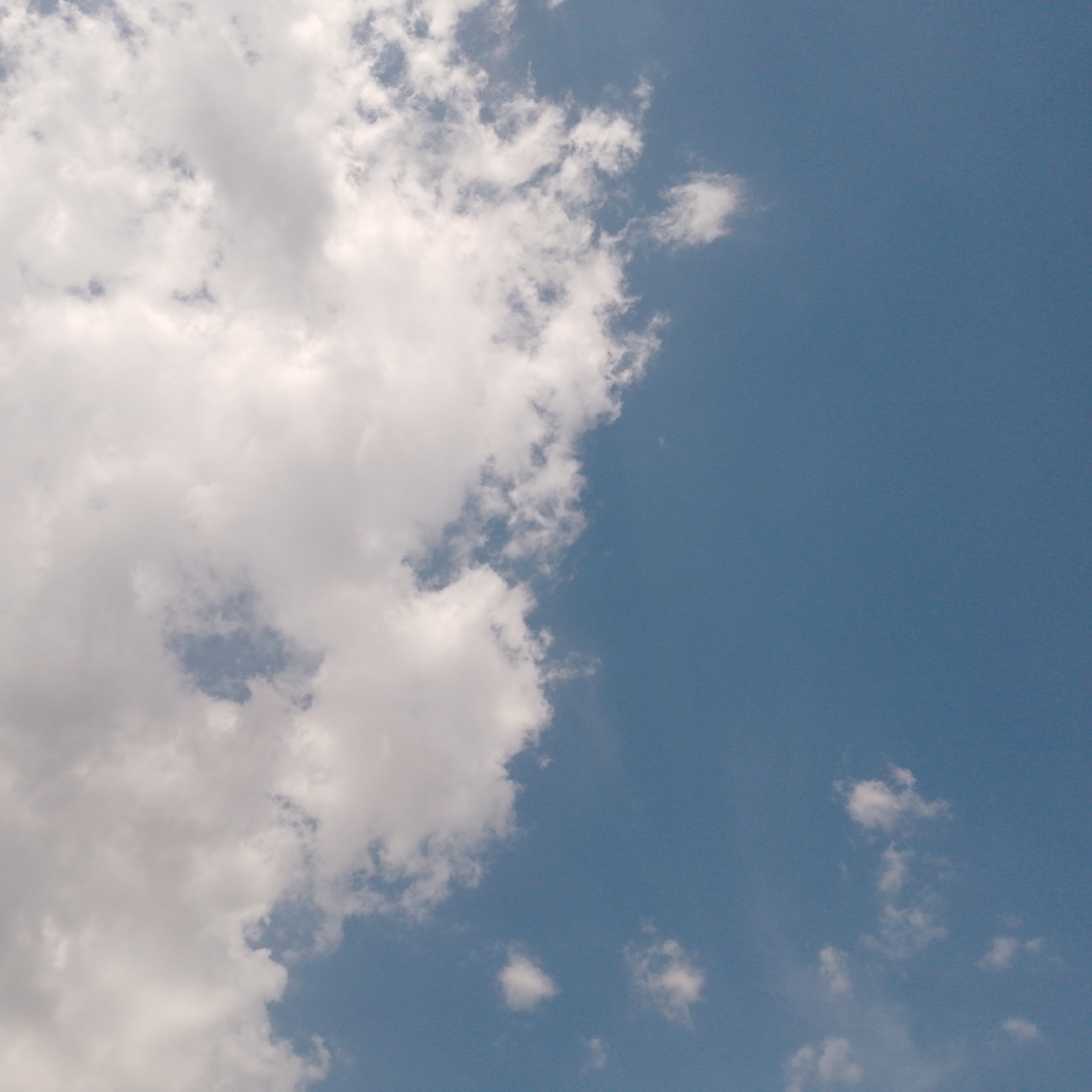 The image shows a view of the sky. The sky is blue with scattered white clouds. The clouds are mostly concentrated on the left side of the image, while the right side is predominantly blue sky. Some small clouds are also visible in the lower portion of the image. The location is Unknown, Unknown.
