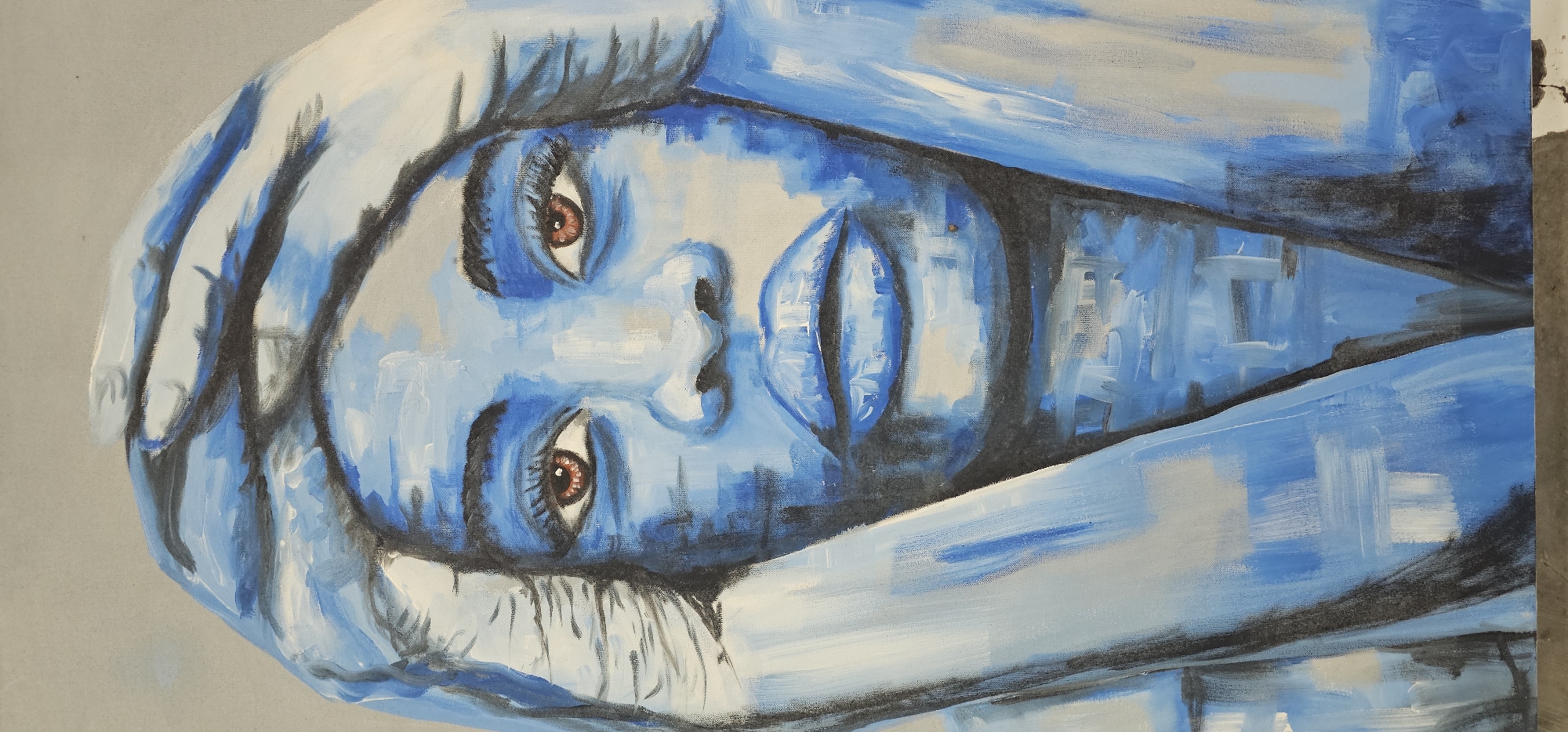 A close-up, portrait-style painting shows a person rendered in shades of blue. The person's face is the focal point, with details such as eyes painted a contrasting brown, and lips defined with lighter blue highlights. Hands, also in blue tones, are positioned around the head, framing the face. The background is a light grey. The painting style is impressionistic with visible brushstrokes. There is no indication of a location in Denpasar, Indonesia, or any city.