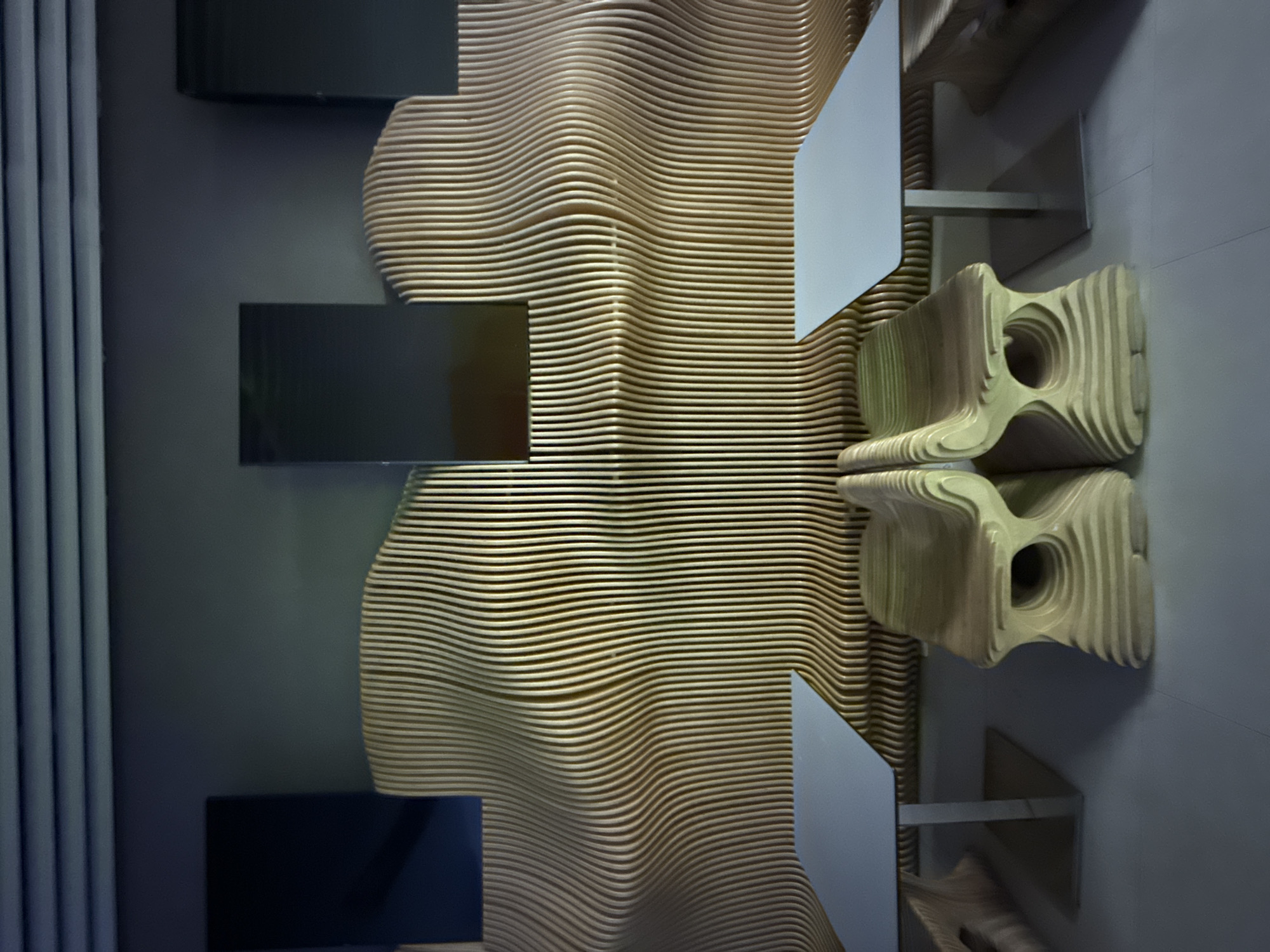 A photograph shows a design element with layered wood strips on a wall, reflected by mirrors in Domodedovo, Russia. The wall has dark panels on the left, and a set of layered wooden chair/sculpture is visible on the right, with metal supports holding up what seems to be a table.