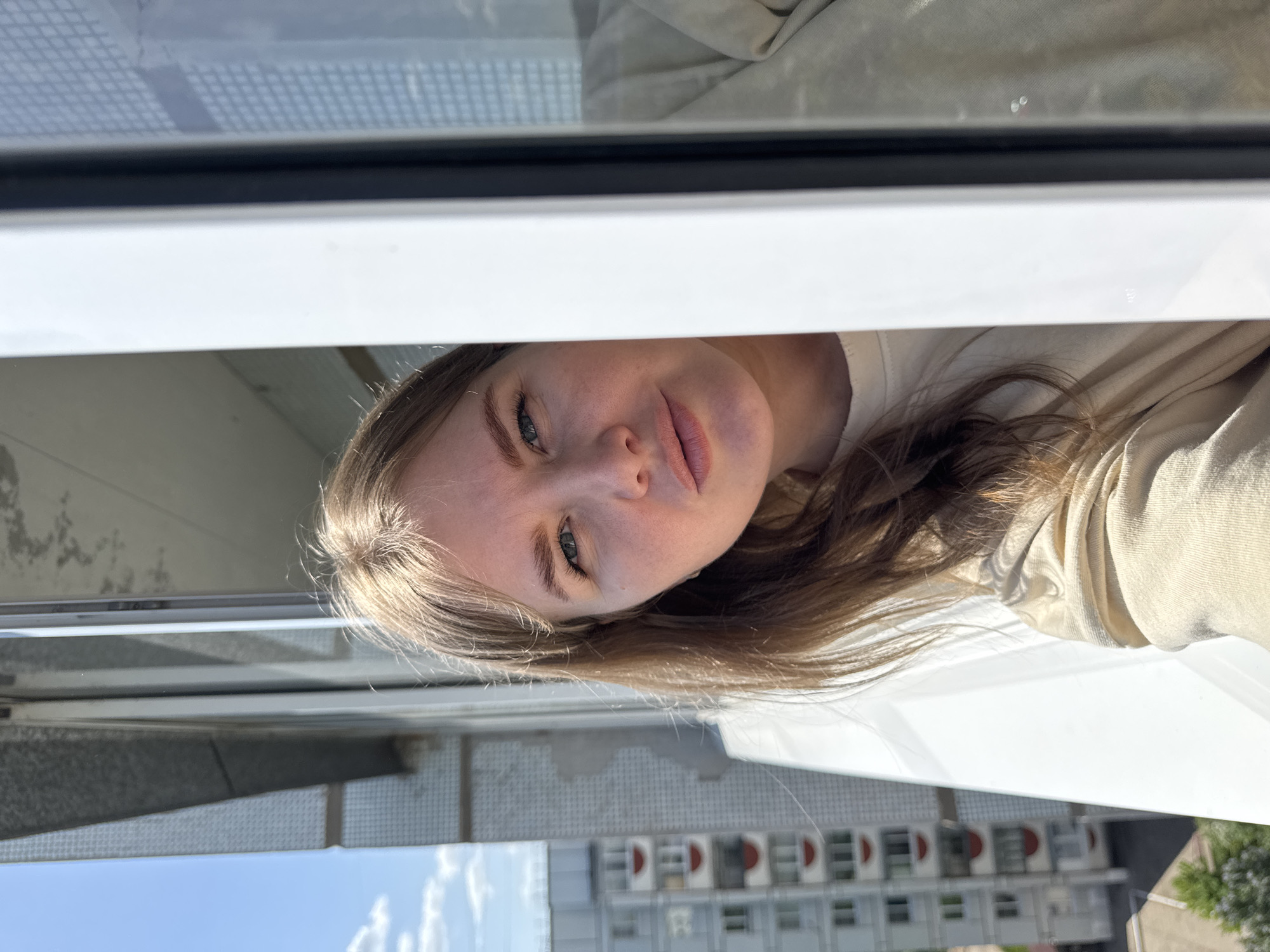 A woman is looking out of a window. The buildings visible outside of the window appear to be in Chaikovsky, Russia.