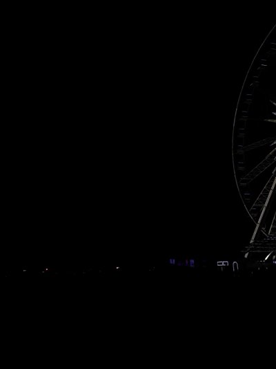At night, a Ferris wheel is seen in the dark with only its structure illuminated. Some small lights are visible in the distance.
The location could be in Indio, United States.