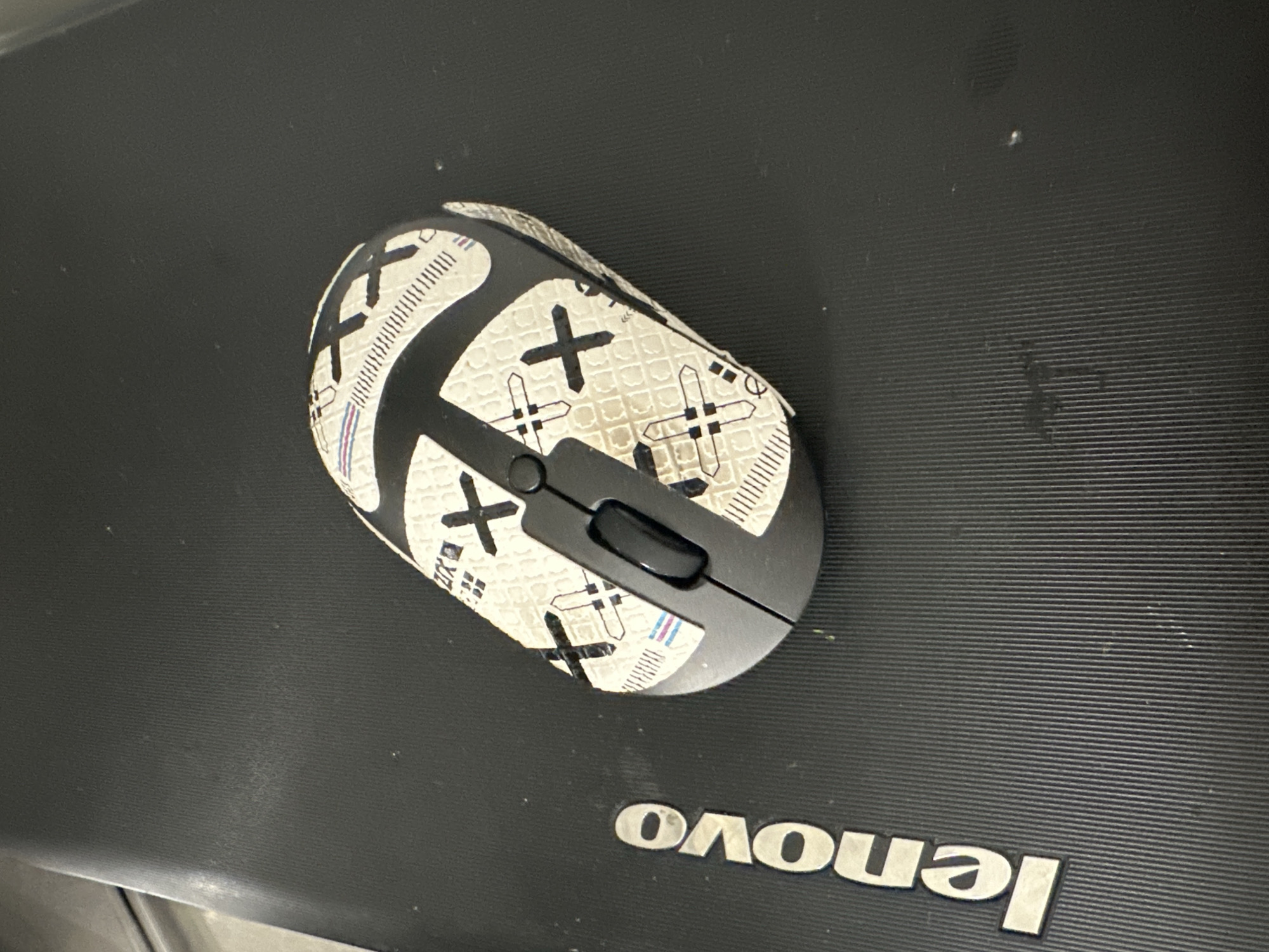 A computer mouse is situated on a black Lenovo laptop. The mouse is white with a pattern of black "X"s and plus signs. The laptop is in Новоглаголево, Russia.