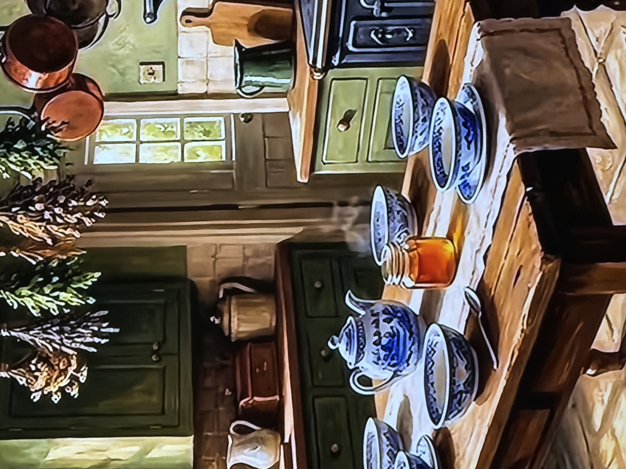 This media file captures a richly detailed, rustic kitchen interior, presented at an angle that rotates the scene ninety degrees clockwise from its natural orientation. The atmosphere is warm and traditional.
On the left side of the scene (which would be the top wall if viewed horizontally), several gleaming copper pots and pans hang. Below them, bundles of dried herbs or flowers are suspended, adding a natural, homely touch. A multi-paned window is visible, through which vibrant green foliage can be seen, indicating daytime and pleasant outdoor conditions. A dark green cabinet is also part of this wall arrangement.
Towards the center and back of the kitchen, a wooden countertop or shelf holds a dark green pitcher. A prominent feature is an old-fashioned black stove or oven, suggesting a functional, traditional cooking space. Beside it stands another green cabinet equipped with drawers.
The main focal point is a long, sturdy wooden table or counter extending diagonally across the image. It is set with an array of blue and white patterned ceramic dishware, including bowls and plates, some stacked or inverted. A decorative blue and white teapot stands ready. A clear glass jar, filled with an amber liquid resembling honey, is placed among the dishes. A simple spoon rests on the table, which is partially covered by light-colored fabric placemats and a darker brown table runner.
Further below the main table, another dark green cabinet is visible, topped with a metallic teapot or kettle, alongside other traditional kitchen items like a brown container and a white pitcher.
The kitchen is unoccupied, exuding a peaceful and inviting ambiance. The natural light filtering through the windows confirms it is daytime. No specific location cues are present within the image, but the style of the decor—featuring wooden furniture, traditional cookware, and green cabinetry—evokes a classic countryside or historical European kitchen aesthetic. No visible text is present in the image.