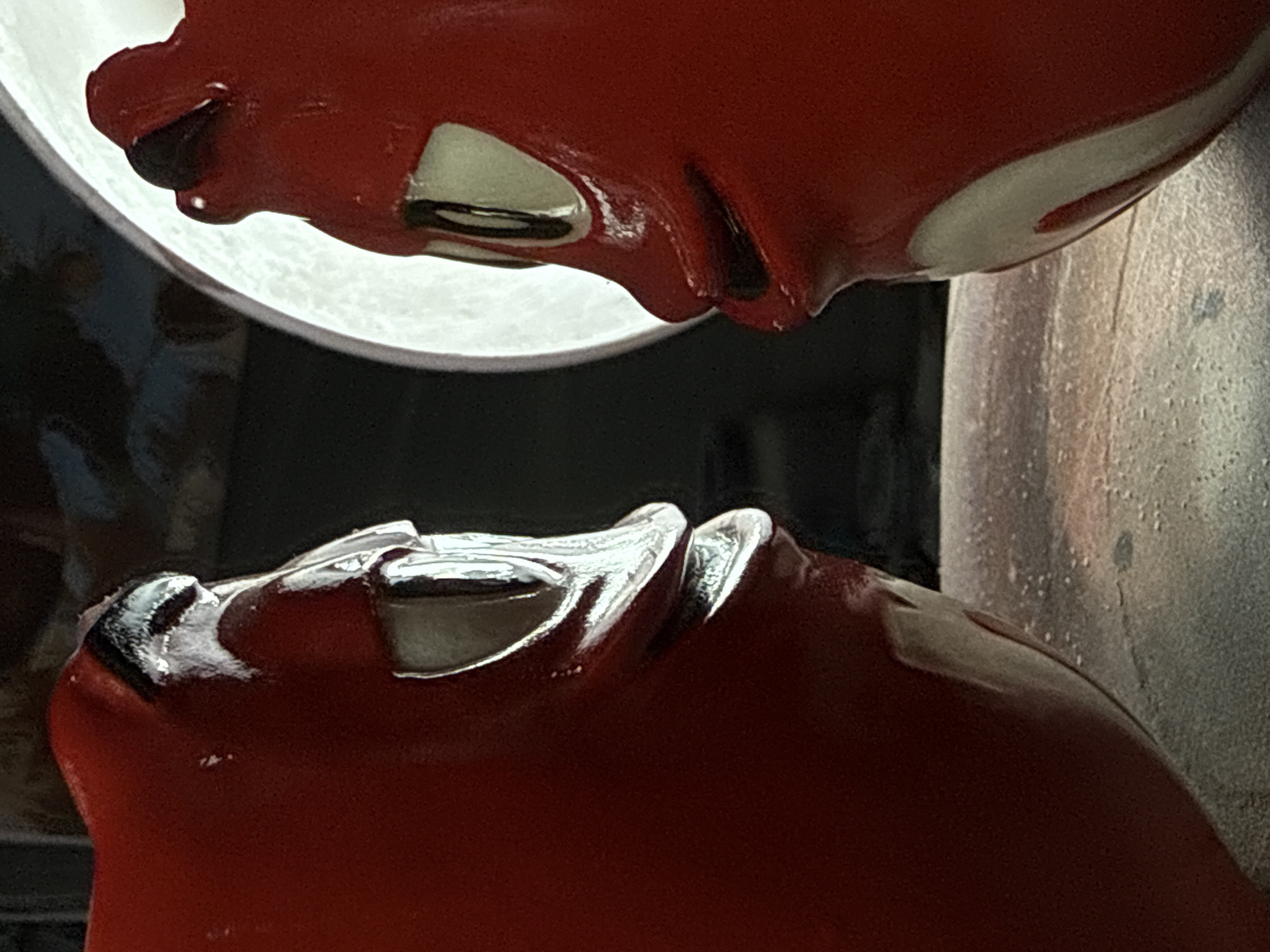The image shows a close-up of two red, stylized human faces. The faces are rendered in a glossy material. The face at the bottom is upright, while the other is positioned above it, seemingly about to touch the lower face.