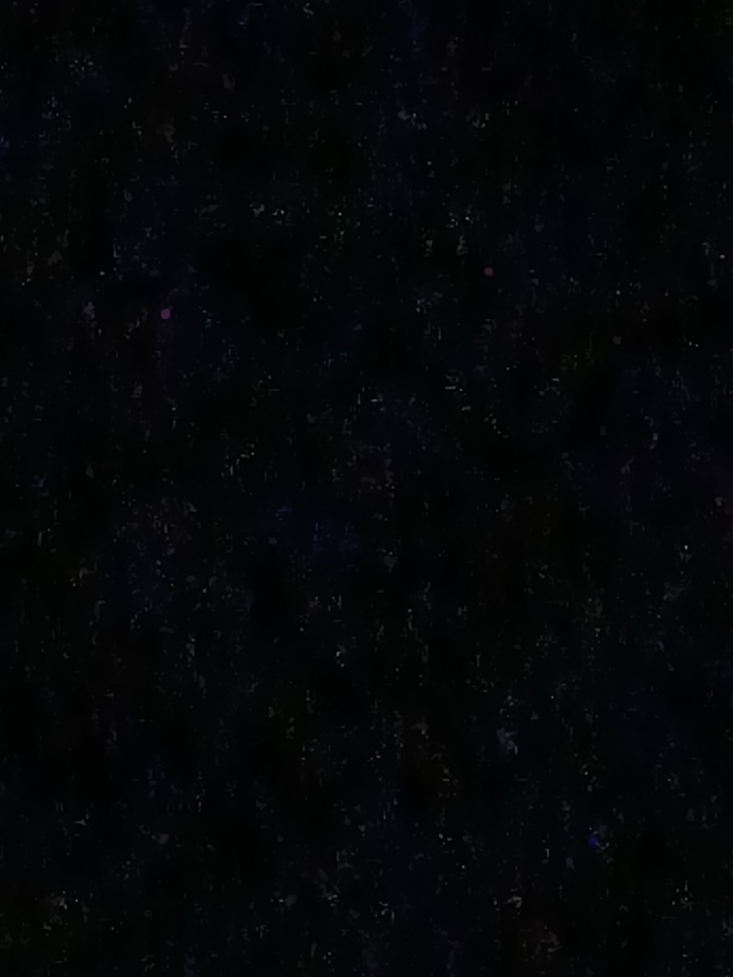 The image is a dark, grainy, and highly abstract depiction of a night sky, possibly with some atmospheric or digital interference. It is predominantly black with scattered specks of white and faint colored hues, suggesting stars or distant light sources. There are no discernible objects, people, or identifiable features that would allow for a forensic description of a scene in Kyzyl-Suu, Kyrgyzstan, or any other location. The image lacks any detail related to urban environments, landmarks, or human activity.