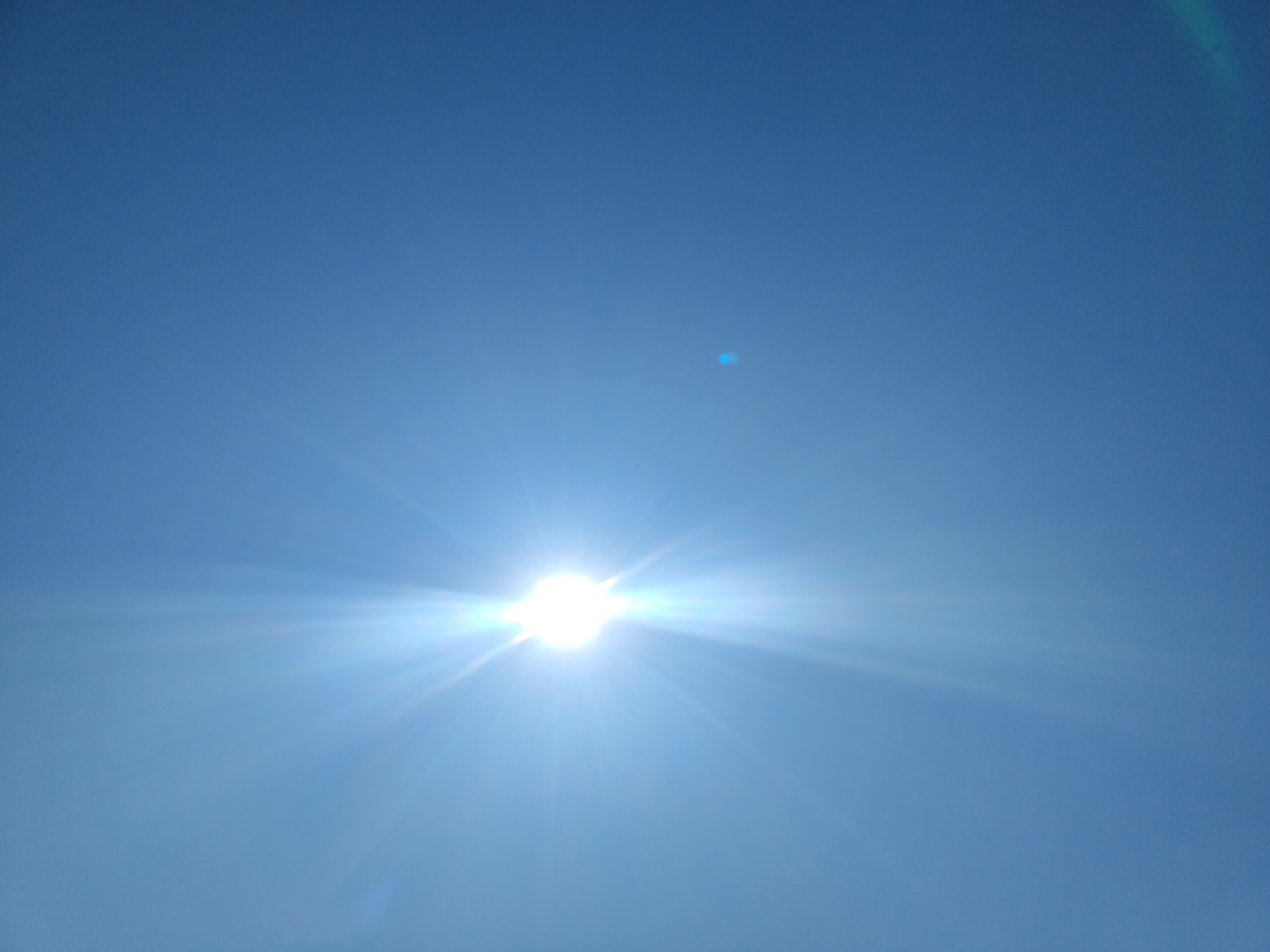 A bright sun shines in a clear blue sky, casting bright rays across the frame. There are no people or objects visible in the image, and the scene is devoid of any activity. The image appears to have been taken outdoors.
