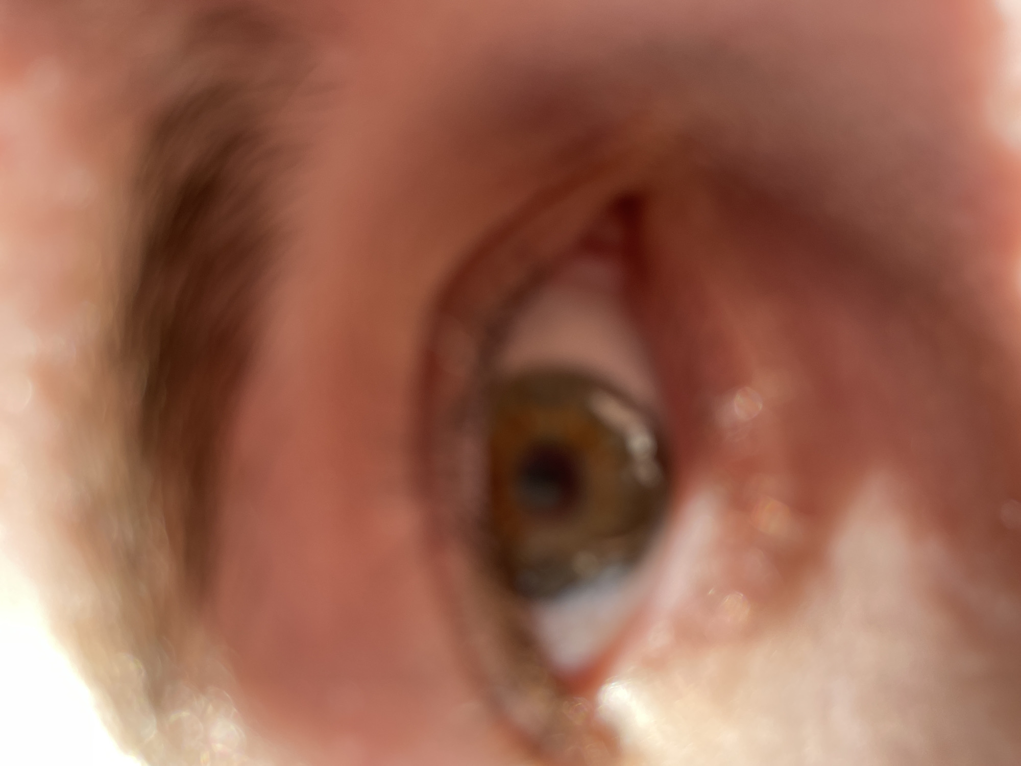 The image is a very close, blurry shot of a human eye. The iris is visible and appears to be hazel in color. Parts of the surrounding skin, eyebrow, and inner corner of the eye are also visible, although they are also out of focus. No information in the image suggests the location is Chaikovsky, Russia.