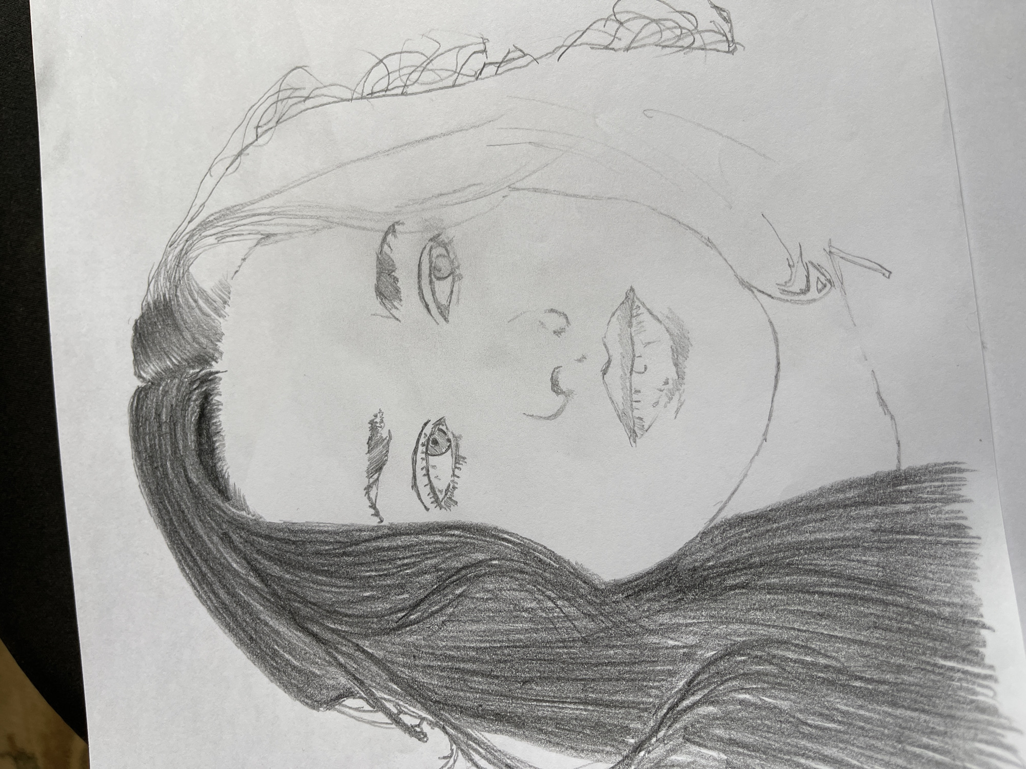 A pencil drawing on white paper shows a woman's face. The top portion of her face has lighter sketching, while the lower portion of her hair is heavily shaded. The drawing is not in Jos, Nigeria, and contains no indication of location.