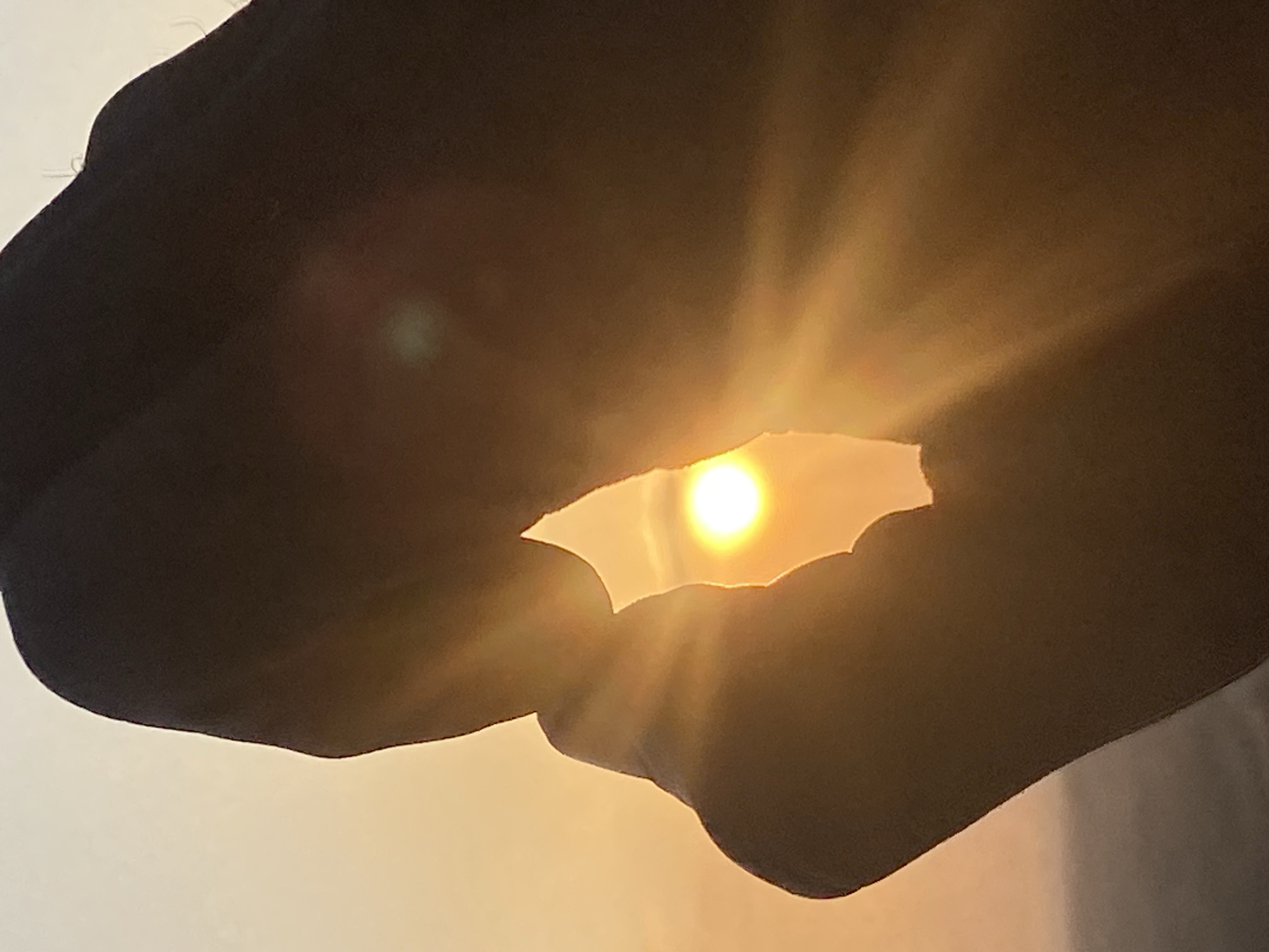 A close-up shot captures a silhouette of hands against a bright sunset, creating a lens flare effect. The hands are positioned to frame the sun, with light rays emanating outwards. The setting appears to be outdoors in Abakaliki, Nigeria, indicated by the warm, hazy sky typical of sunset in the region.