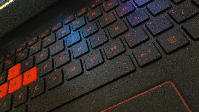 The image shows a close-up of a black laptop keyboard. The keys are black with red lettering, and the keyboard has a textured surface. The keys are arranged in a standard QWERTY layout. The image is taken from a slightly elevated angle, and the keys in the bottom left corner are in focus, with the remaining keys gradually becoming blurry towards the top right corner. The image was taken in Magelang, Indonesia, at coordinates -7.479 latitude and 110.222 longitude. The laptop keyboard is in use, with several keys depressed. The keyboard is illuminated by a light source from the top left. There is a touchpad in the bottom right corner.