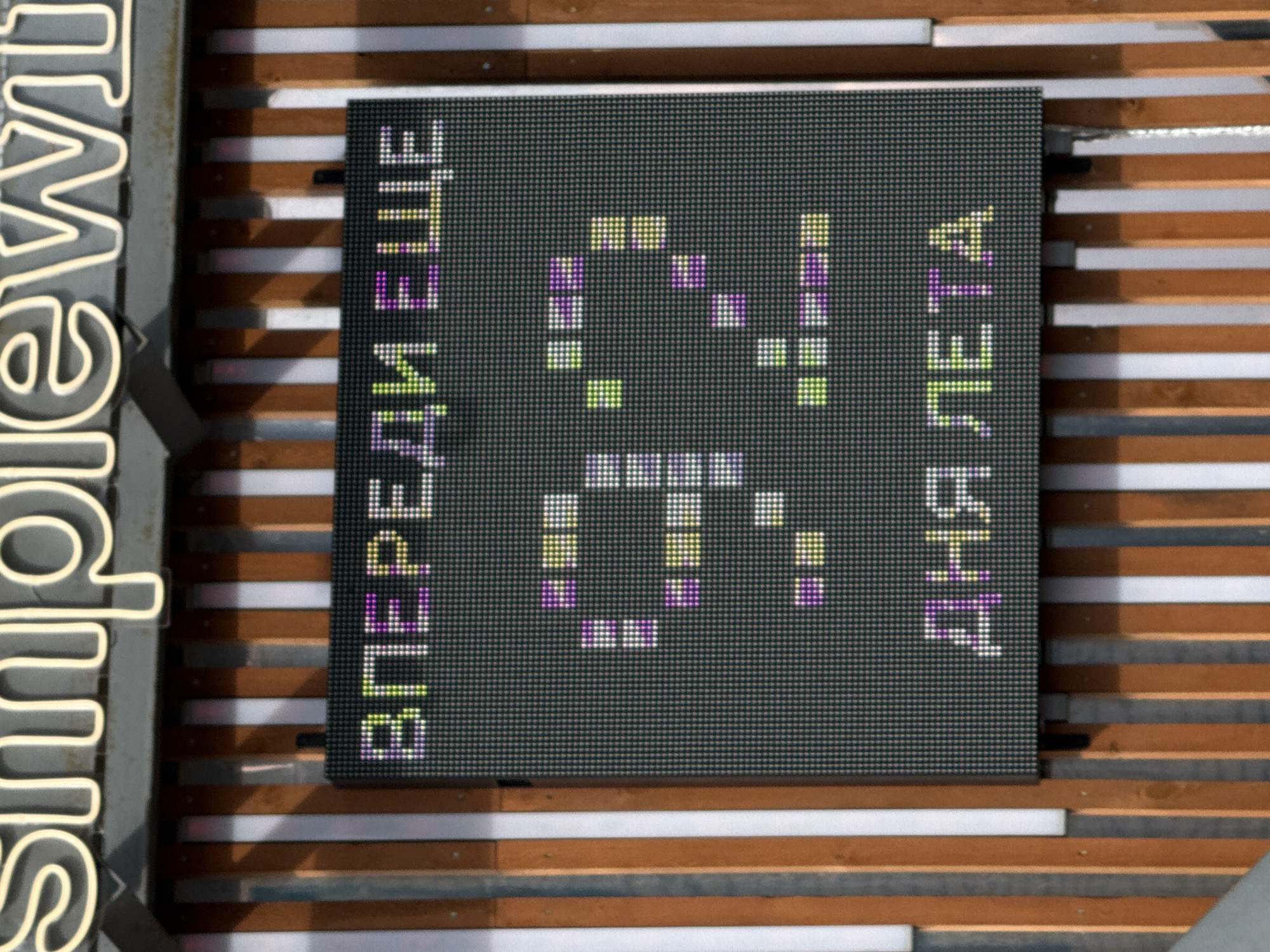 A close-up, overhead shot shows a digital display mounted on a striped, wooden-look facade. The display reads in Russian, "Впереди еще 62 дня лета", which translates to "62 days of summer ahead". Part of a vertically-oriented sign with the text "Maldins" is visible on the left, indicating the location of this image in St. Petersburg, Russia.