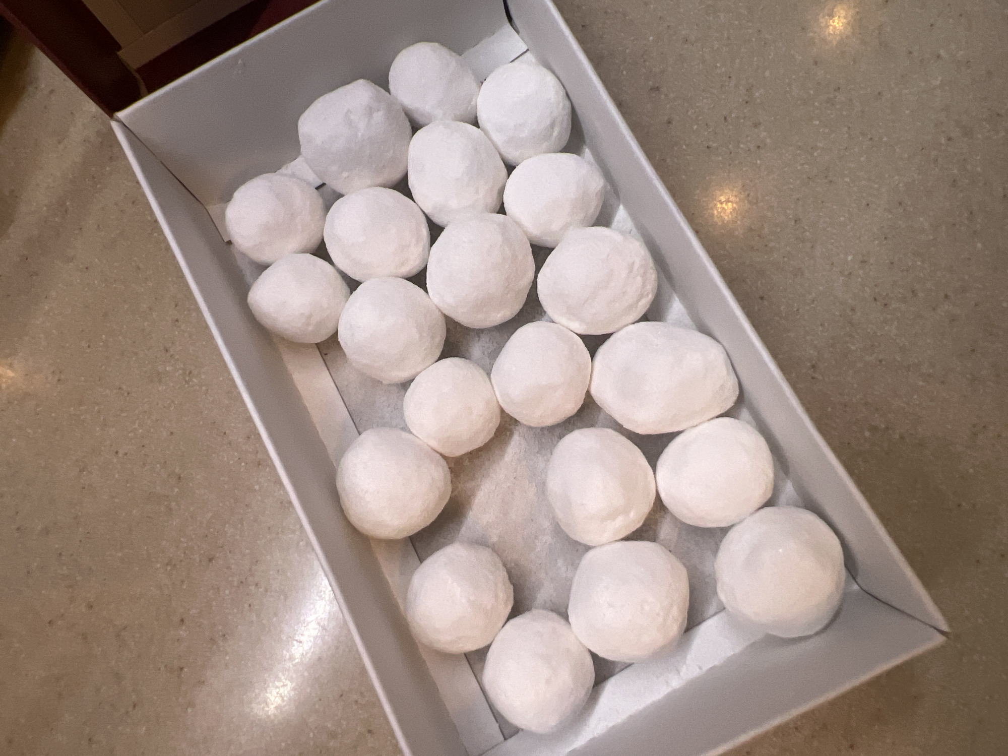 A white rectangular box contains approximately twenty-two white, spherical objects, possibly confections or decorative items. The box is positioned on a speckled, beige countertop. The lighting suggests an indoor environment, with some subtle reflections on the countertop. No people, animals, or specific landmarks of Saint Petersburg, Russia are visible.