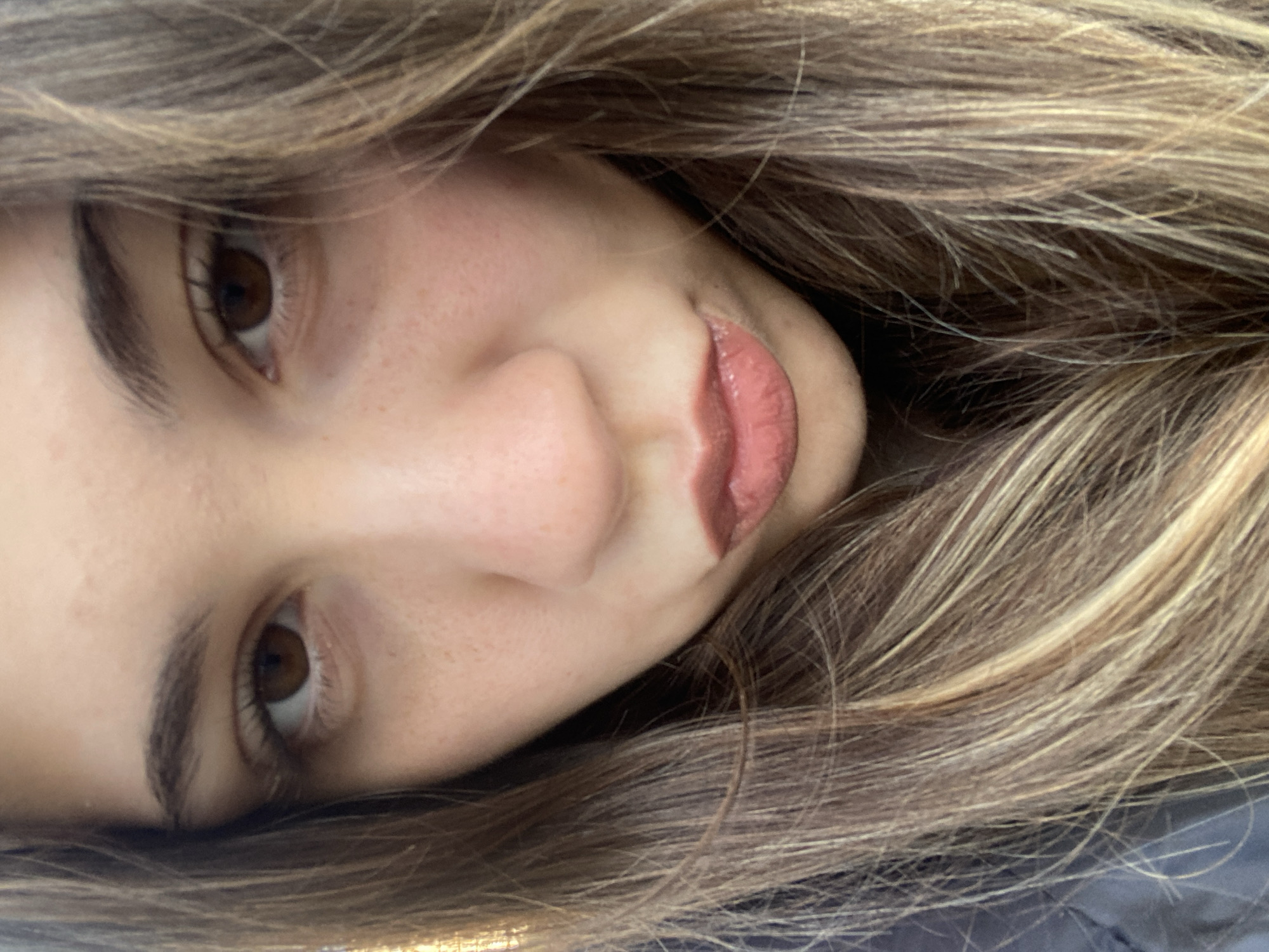 A close-up portrait of a woman with light brown hair, brown eyes, and light skin. Her face is angled slightly to the right. She has freckles and is wearing lipstick. No location information is discernible from the image.