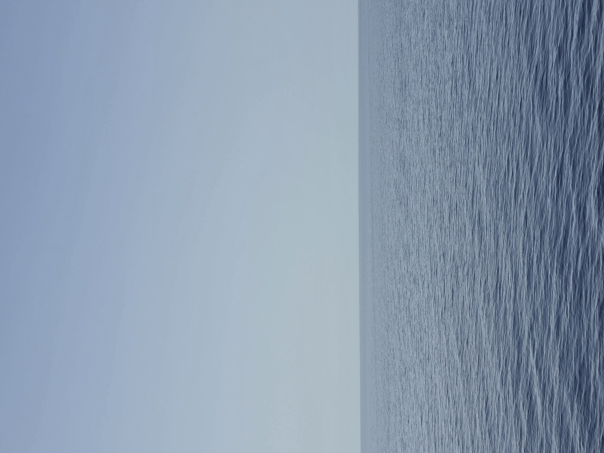 The image depicts a serene seascape with a clear, pale blue sky meeting a calm, deep blue ocean at the horizon. The water's surface is gently rippled, suggesting a tranquil atmosphere. The scene is devoid of any human presence or man-made objects, presenting a vast expanse of natural elements. The location is identified as Santa Ponça, Spain, a coastal town known for its beaches and marina. The photograph captures the essence of a peaceful day at sea, highlighting the simplicity and immensity of the ocean and sky.