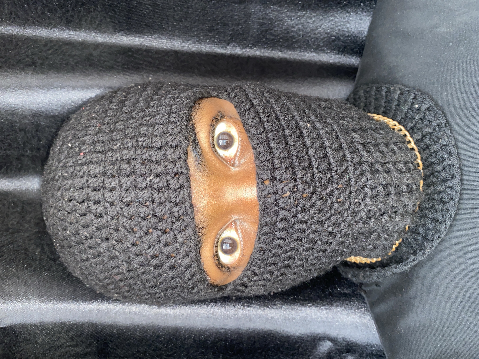 The image shows a person wearing a black knitted balaclava, with only the eyes and a small portion of the nose visible. The person is lying down on a dark, ridged surface, possibly the bed of a truck or some similar vehicle. The background is blurred and dark. No information indicates this photograph was taken in Barakin Akawo, Nigeria.