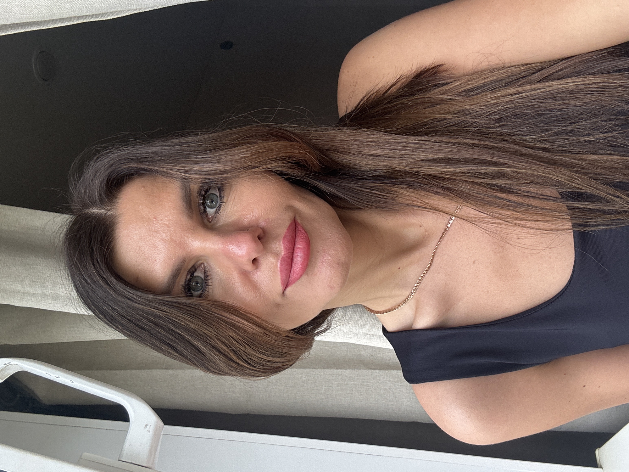 A woman with long brown hair is looking into the camera. She is wearing a black top and a gold necklace. The background is a neutral tone. There is no indication in the image itself that it was taken in the city of Chaikovsky, Russia.