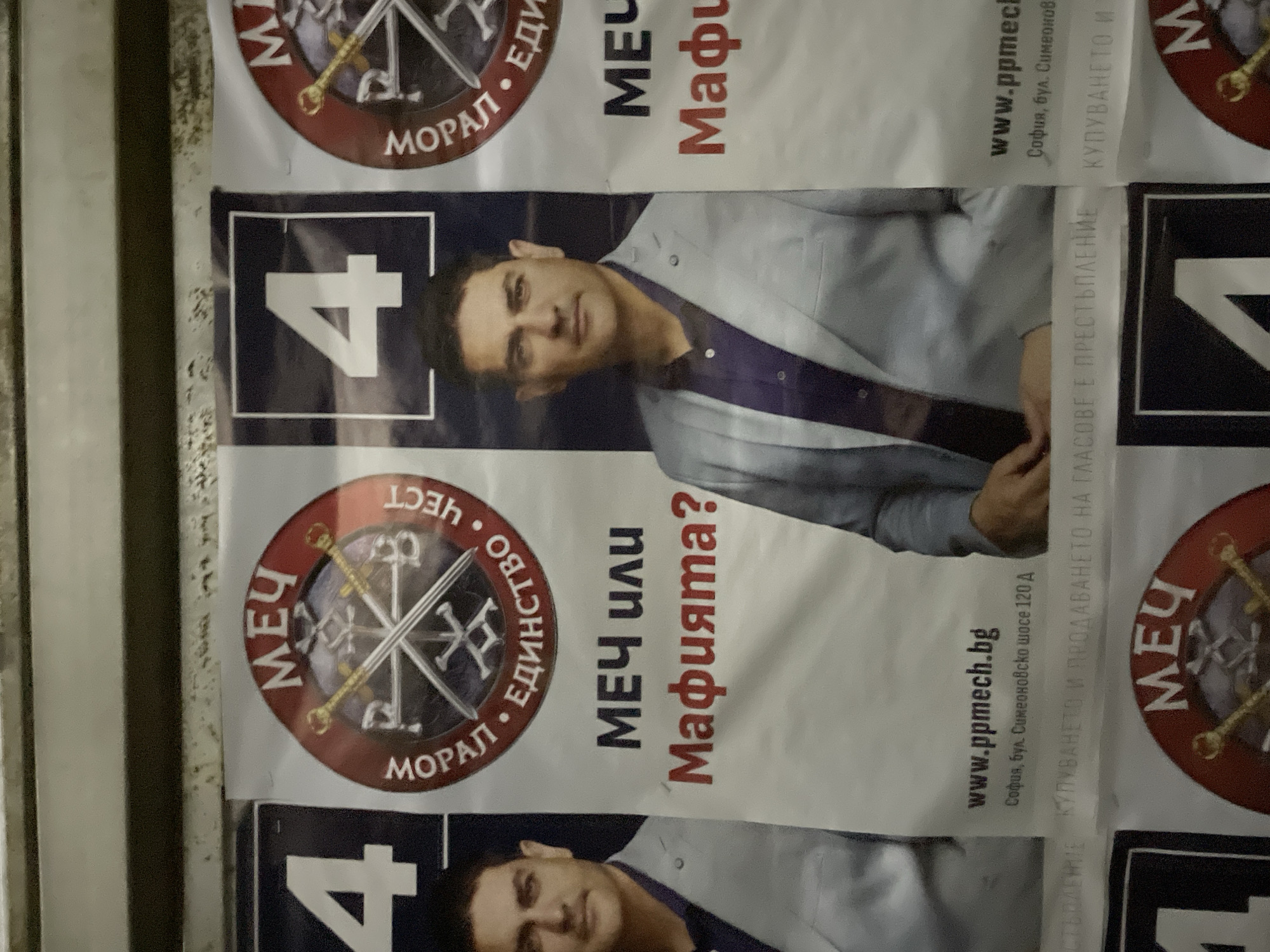 The image shows campaign posters for a political party or individual, possibly in Sofia, Bulgaria. The posters feature a man in a light grey suit over a dark purple shirt and display the number "4". The acronym "МЕЧ" is prominent, accompanied by the phrase "МЕЧ или Мафията?" (Sword or Mafia?). The symbol includes swords and a cross. The website "www.ppmech.bg" is listed along with the address "София, бул. Симеоновско шосе 120 A" (Sofia, Simeonovsko Shose 120 A). A small note at the bottom of the posters reads "КУПУВАНЕТО И ПРОДАВАНЕТО НА ГЛАСОВЕ Е ПРЕСТЪПЛЕНИЕ" (Buying and selling votes is a crime). The posters are lined up, suggesting they are part of a larger campaign display.