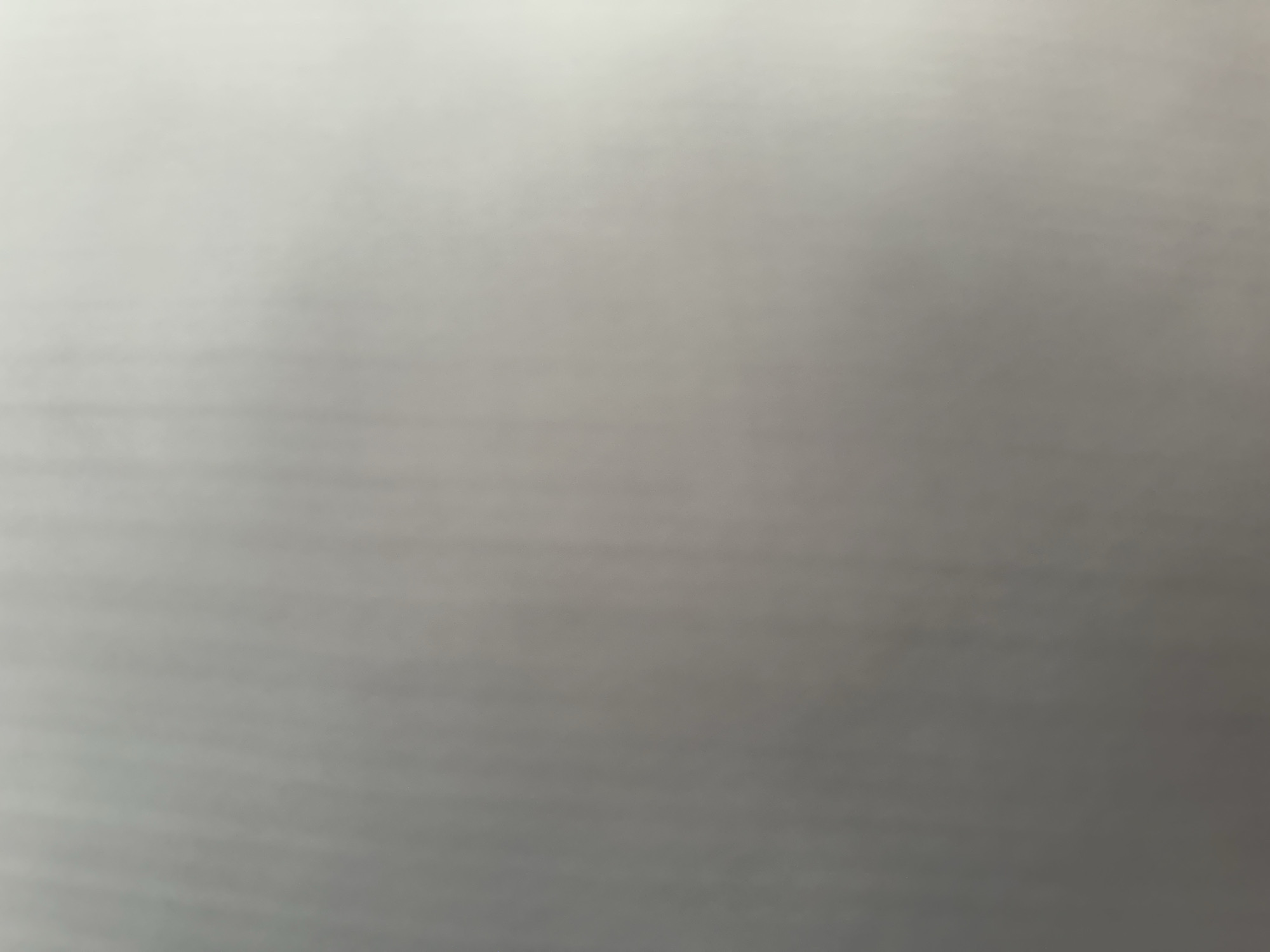 The image is a blurry, grey abstract background. There are no discernible subjects, objects, scenes, activities, or events. There are no notable details such as time of day, weather, location cues, or emotions. There is no visible text. The image appears to be a close-up of a textured surface, possibly paper or fabric, with horizontal lines visible due to the blur. The lighting is even and diffused, creating a gradient from lighter grey at the top to darker grey towards the bottom.