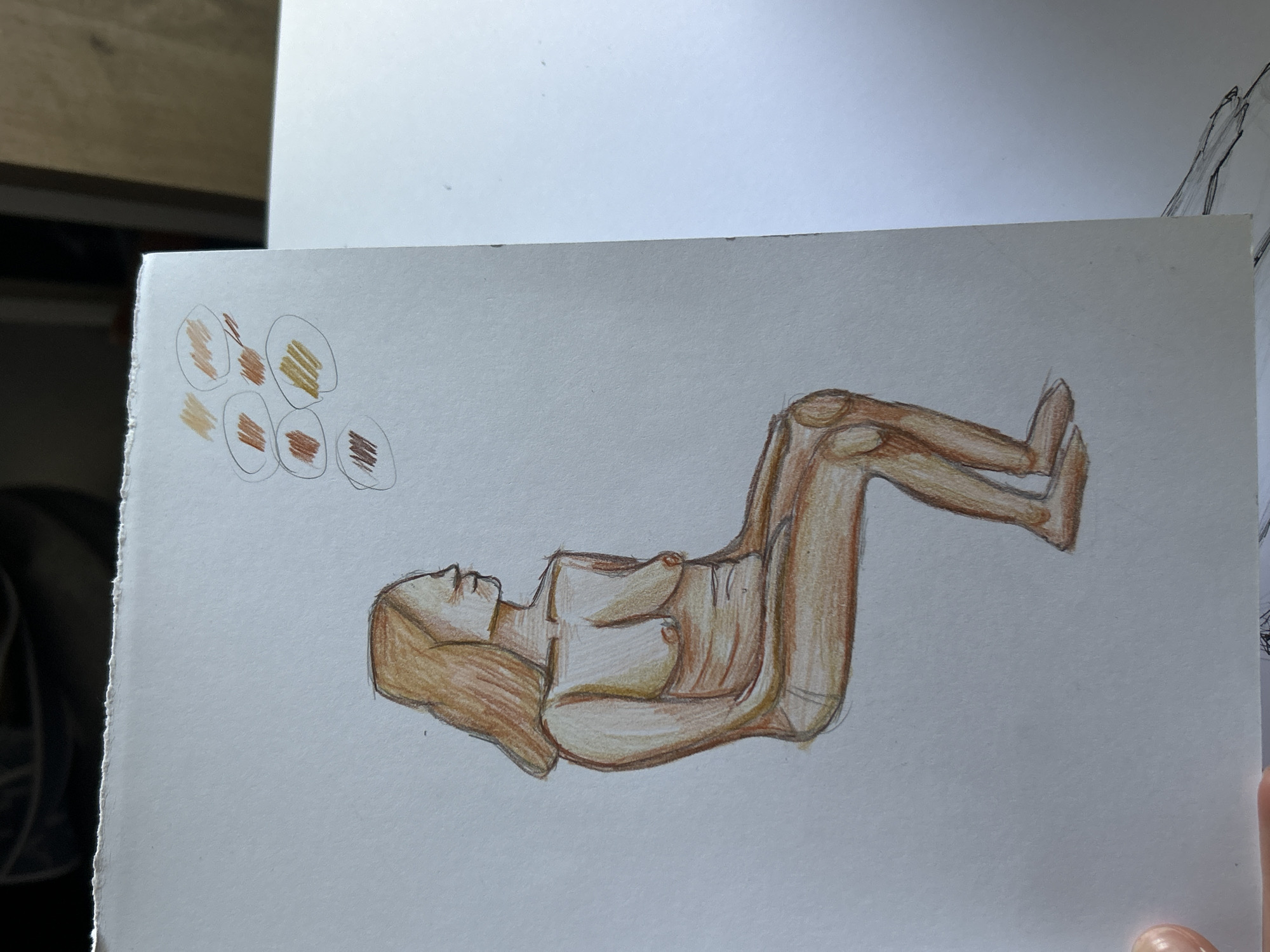 A colored pencil drawing on white paper depicts a nude female figure lying on her back with knees bent and raised. A series of color swatches is in the upper left corner of the drawing. The subject is not depicted in Sofia, Bulgaria.