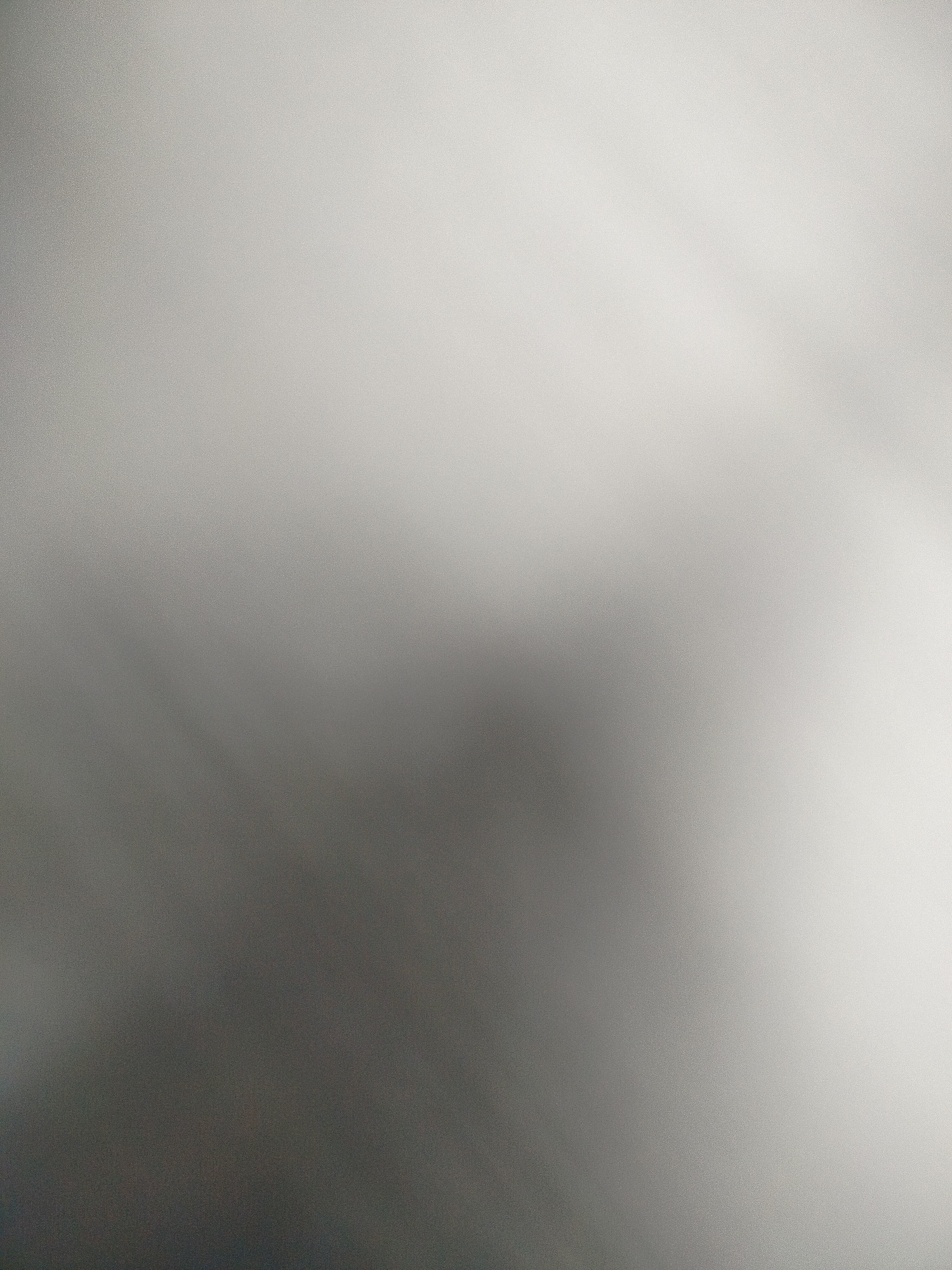 The image is a blurred, close-up shot, predominantly gray in tone, with a grainy texture. The bottom left corner is darker, transitioning to a lighter shade towards the top right. There are no discernible objects, subjects, people, or actions visible within the frame. The lack of identifiable elements prevents any contextual information, including the location within Yerevan, Armenia, from being determined. The environment is simply an out-of-focus, indistinct gradient of grayscale.