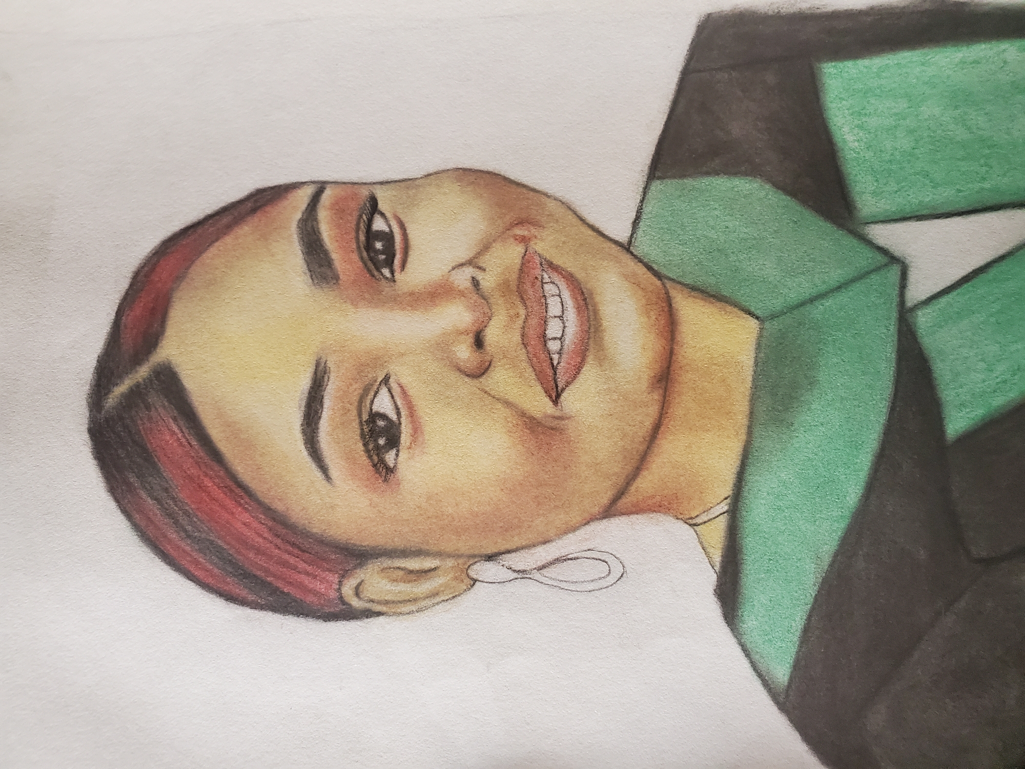 The media file features a colored pencil portrait of a person, likely a woman, depicted with a cheerful and engaging expression. The subject has a light to medium brown complexion, dark eyes, and dark, well-defined eyebrows. Her hair is dark brown with prominent reddish-brown streaks or highlights, particularly visible on the side of her head.
She is shown with a wide, open-mouthed smile, revealing her teeth, and her lips are colored in a reddish-pink shade. A simple, loop-shaped earring is visible on her right ear (viewer's left). The subject is wearing a garment, possibly a jacket or top, rendered in dark gray or black, which features a vibrant green collar or lapel with a distinct, somewhat geometric pattern.
The drawing is presented at an angle, suggesting a tilt of the subject's head or the artwork itself. The background is a plain, untextured white, allowing the focus to remain on the portrait. Visible texture from the colored pencils and paper is evident throughout the artwork, especially in the skin tones and the green sections of the clothing. No specific activity or event is taking place beyond the subject posing for the portrait. There is no visible text in the image. This artwork is from Mararaba, Nigeria.