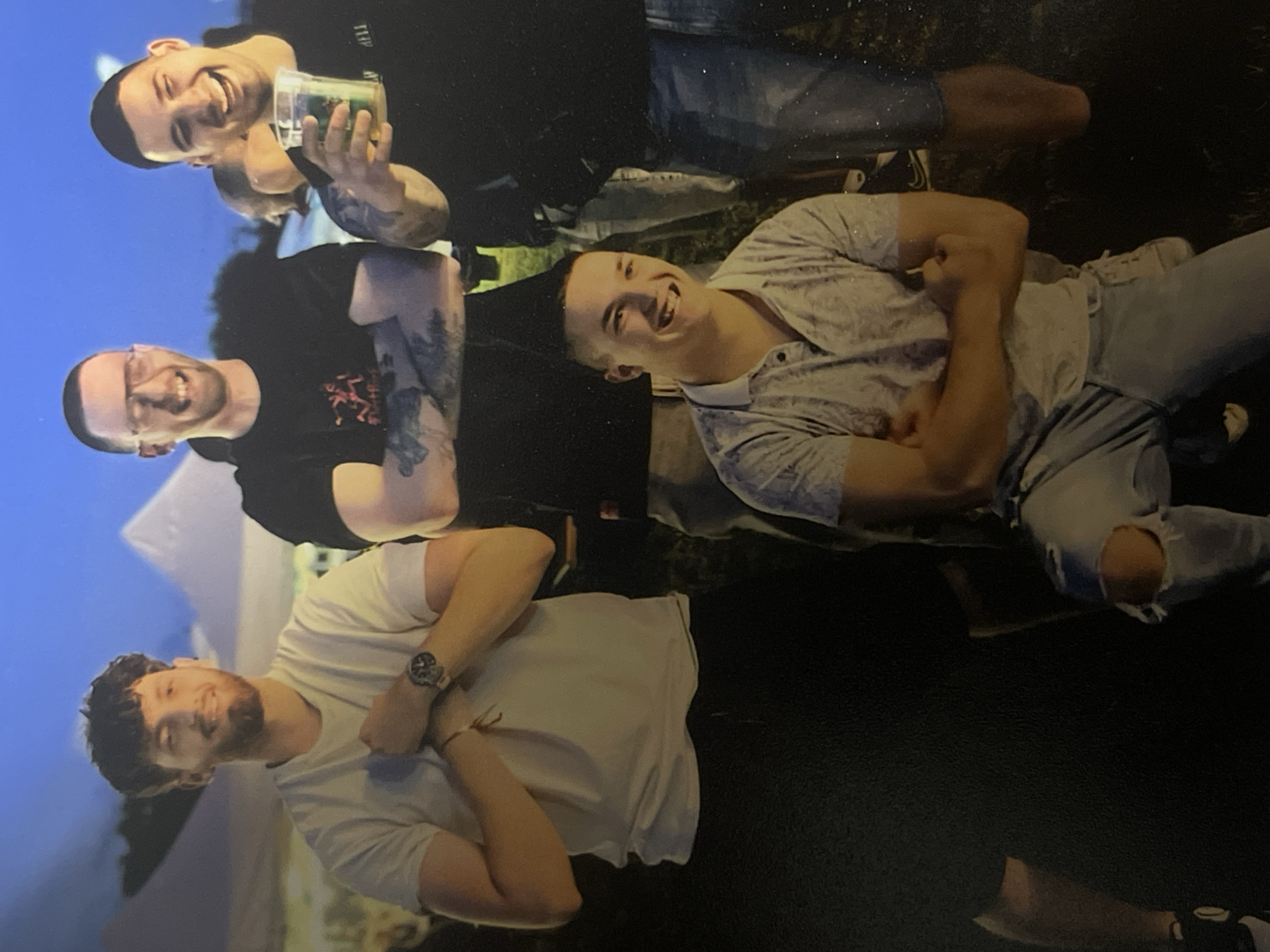 The image shows a group of four men posing together. The man at the top is holding a clear plastic cup filled with a green substance. All four men are smiling and appear to be in a social setting. The backgrounds suggests that the photo was taken at night. I cannot definitively determine the location as Sofia, Bulgaria based on the image provided.