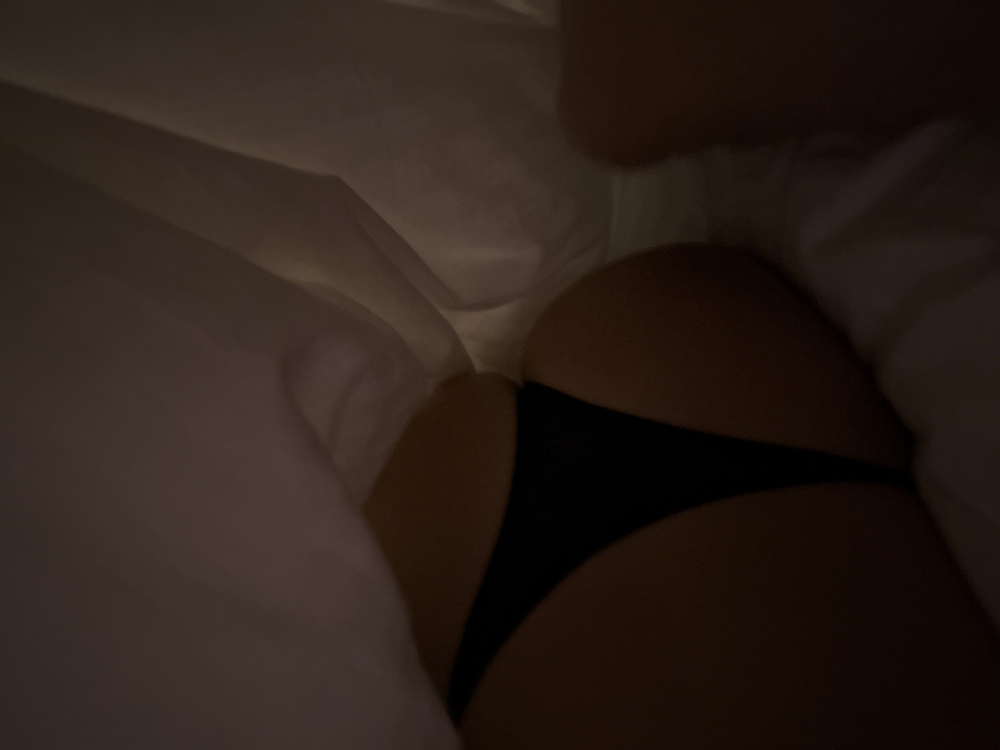 A close-up shot shows a person's buttocks wearing a black thong underwear. The person is under white sheets. The location is unknown.