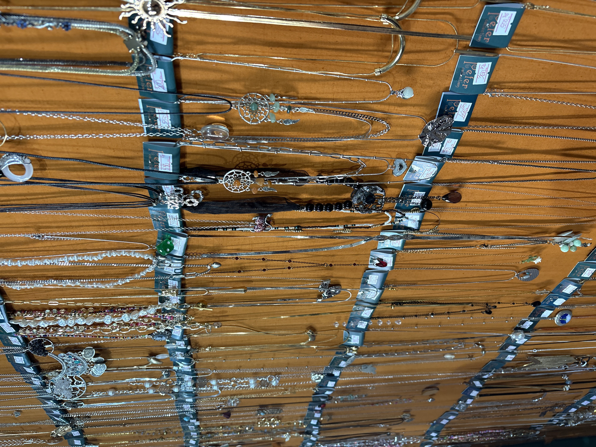 The image displays a collection of necklaces hanging on a display rack. The necklaces vary in style, material, and length, featuring pendants, chains, and beads. Price tags are attached to the display, and the necklaces appear to be for sale. The location is identified as Kragujevac, Serbia.