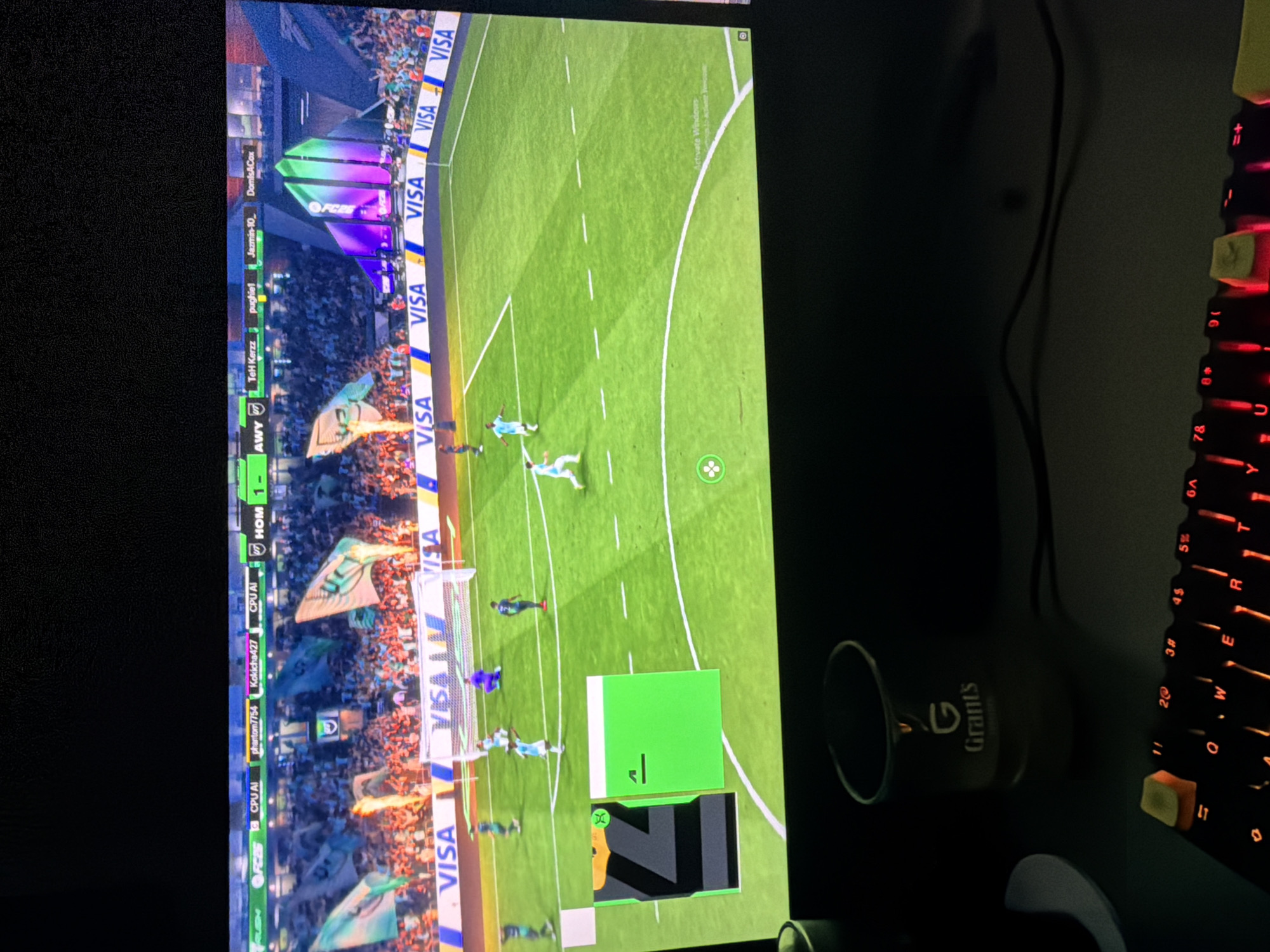 The image shows a computer screen displaying a FIFA 23 game, with a soccer match in progress. The home team score is 1, and the away team score is unknown. Various usernames are visible on the side of the screen, suggesting online multiplayer. To the right of the screen is a mechanical keyboard with illuminated red keys. A coffee mug labeled "Grant's" is positioned next to the keyboard. The background is dark, indicating a dimly lit environment. The location in Pirgovo, Bulgaria, is not apparent from the image.
