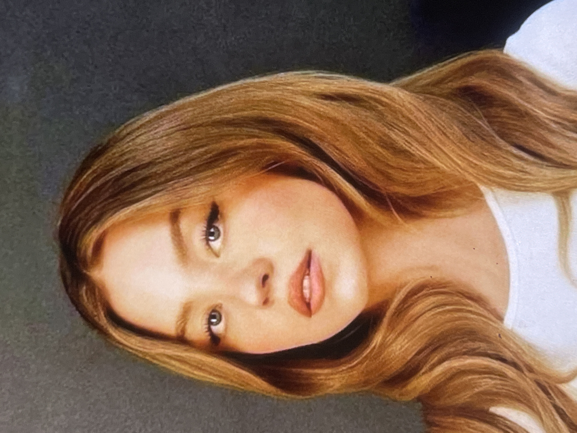 This media file displays a portrait of a young woman, likely an artwork such as a colored pencil drawing or pastel painting, judging by the visible texture and artistic rendering. The image is oriented with the woman's head tilted significantly to the right.
The primary subject is a young woman with fair skin, long, wavy light brown or blonde hair, and light-colored eyes. Her expression is serene and direct, with her lips slightly parted. Her hair is a prominent feature, depicted with fine strands and natural highlights, cascading around her face and shoulders. She appears to be wearing a white garment, possibly a top or t-shirt, visible on the right side of the frame.
The background is a simple, dark gray or charcoal color, providing a stark contrast that highlights the subject. There are no other discernible objects or specific scene elements. The lighting appears soft and even, accentuating her facial features without harsh shadows. There is no activity taking place beyond the static pose for the portrait. No text is visible in the image. No specific time of day, weather, or location cues are evident within the visual content.