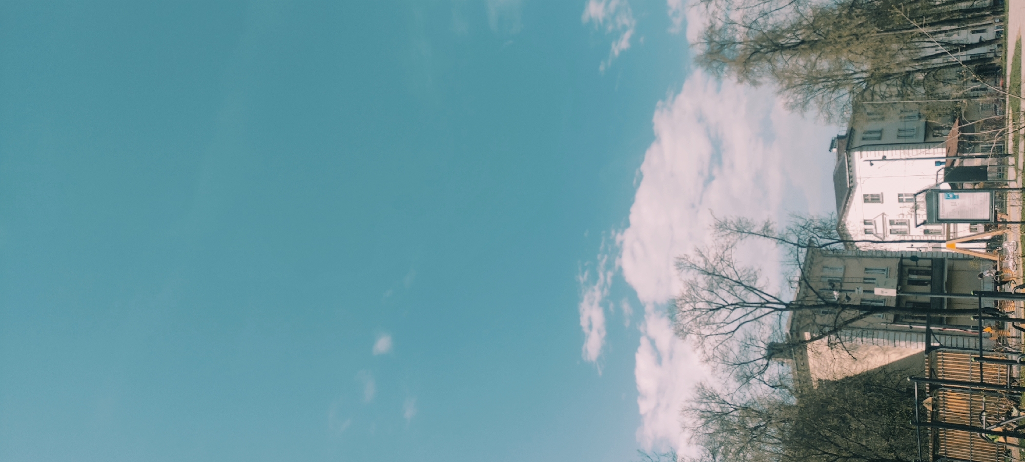 The image shows a building, trees, and a sky with clouds, possibly located in Fryazino, Russia. The building is white with windows, and there is a sign in front of it. The sky is blue with white clouds.