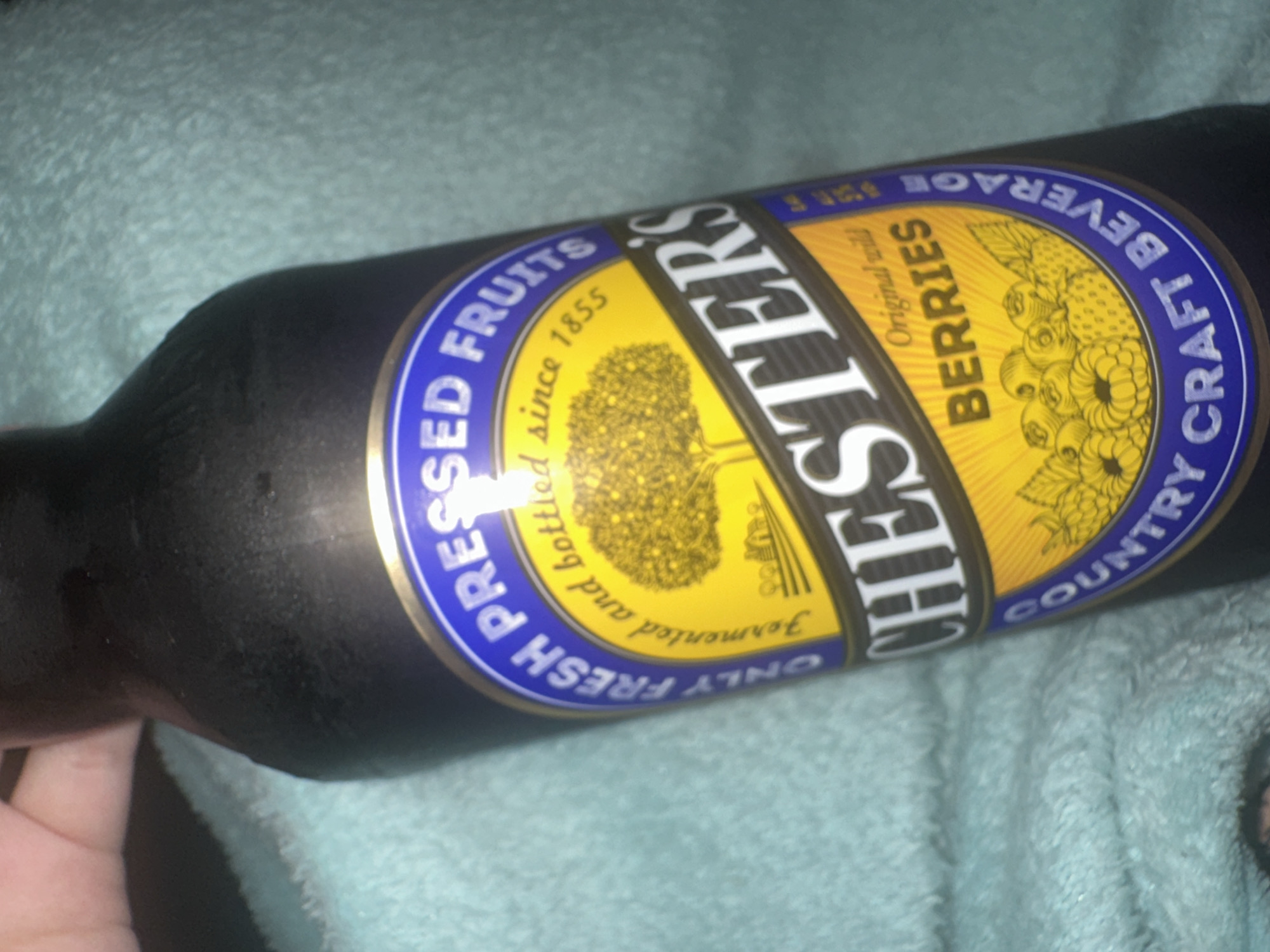 A close-up image shows a bottle of Chester's Original Wild Berries Country Craft Beverage. The bottle is dark and appears to be cold, with condensation visible. The label features a yellow and blue design with the brand name "CHESTER'S" prominently displayed. The label also indicates the beverage is made from "ONLY FRESH PRESSED FRUITS" and "fermented and bottled since 1855." The image does not contain information about the location, so it is not possible to tell if this is taken in the city of Moscow, Russia.