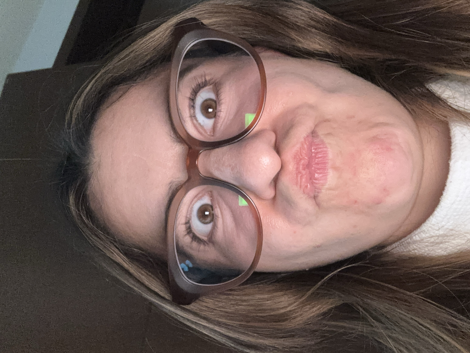 A close-up, rotated image shows a woman wearing glasses. Her eyes are brown. The reflection in her glasses shows a blue tint in the lower left. Her lips are slightly pursed. She appears to have a slight blemish on her right cheek. Her hair is brown with blonde highlights. The background is indistinct. There is no information in the image to determine its location in the city of Puebla, Mexico.