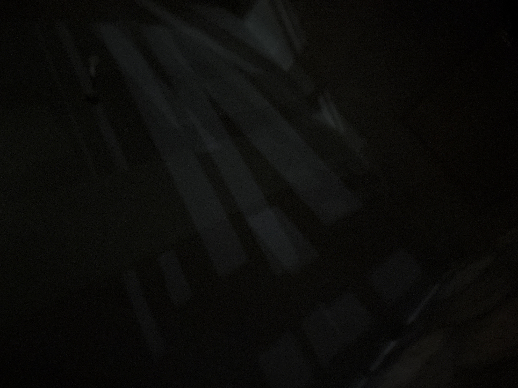 The image shows a dark, dimly lit interior space. There are patterns of light and shadow cast across the surfaces, possibly from window blinds or a patterned window. The light creates strong contrasts. The location is not discernible from the image. There are no visible people or objects that would identify a specific location in Krasnoyarsk, Russia. The lighting suggests it might be nighttime or a room with limited external light.