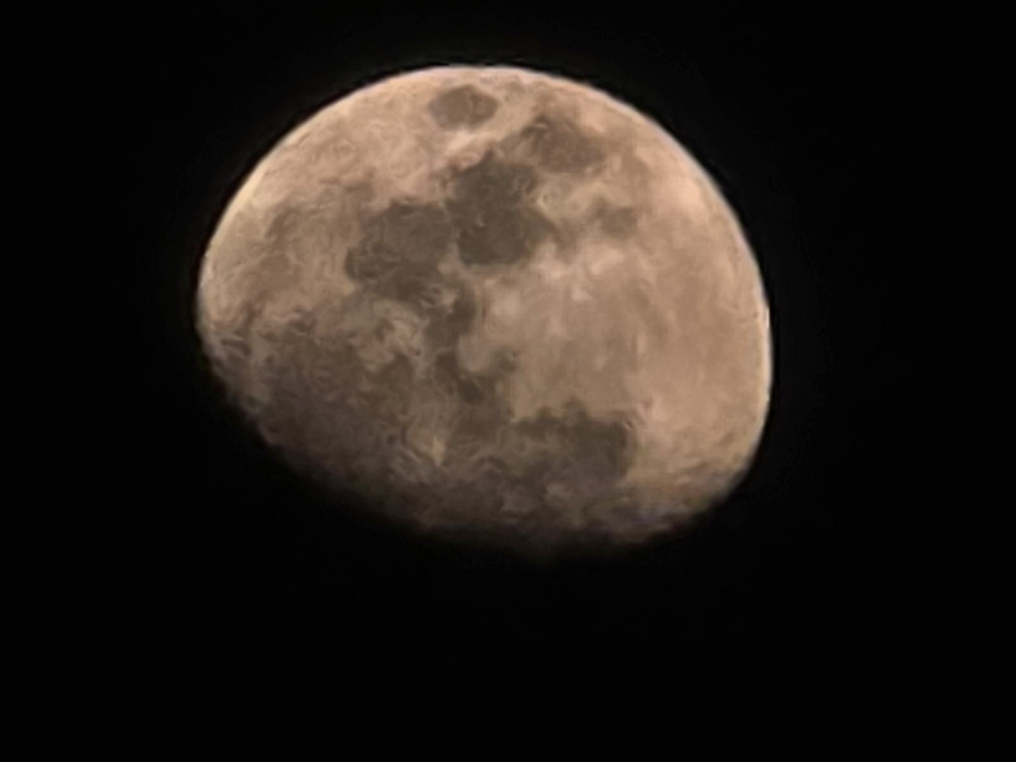 The image is a close-up, out-of-focus photograph of the moon against a black background. The moon is partially illuminated, with a crescent of light visible on the right side and a larger, shadowed area on the left. The surface of the moon shows visible craters and other topographical features, appearing in shades of brown and gray. There are no people, objects, or environmental details suggesting a specific location in Yambol, Bulgaria.