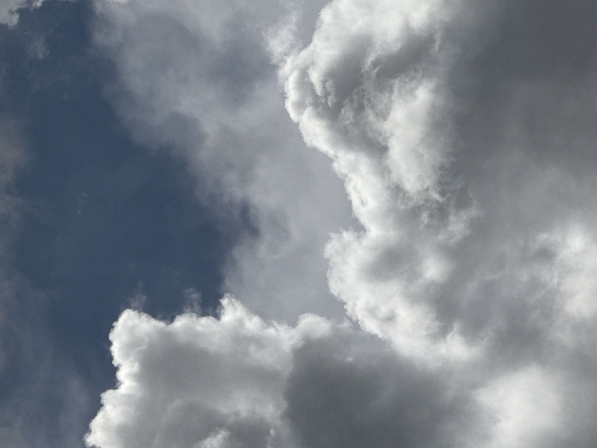 The image shows a view of the sky, dominated by clouds. The lower left corner reveals a patch of dark blue sky, indicating a break in the cloud cover. The clouds are predominantly white and gray, with varying degrees of density. There are no people, objects, or actions visible in the image. The specific location in Strazhitsa, Bulgaria cannot be determined from this image.