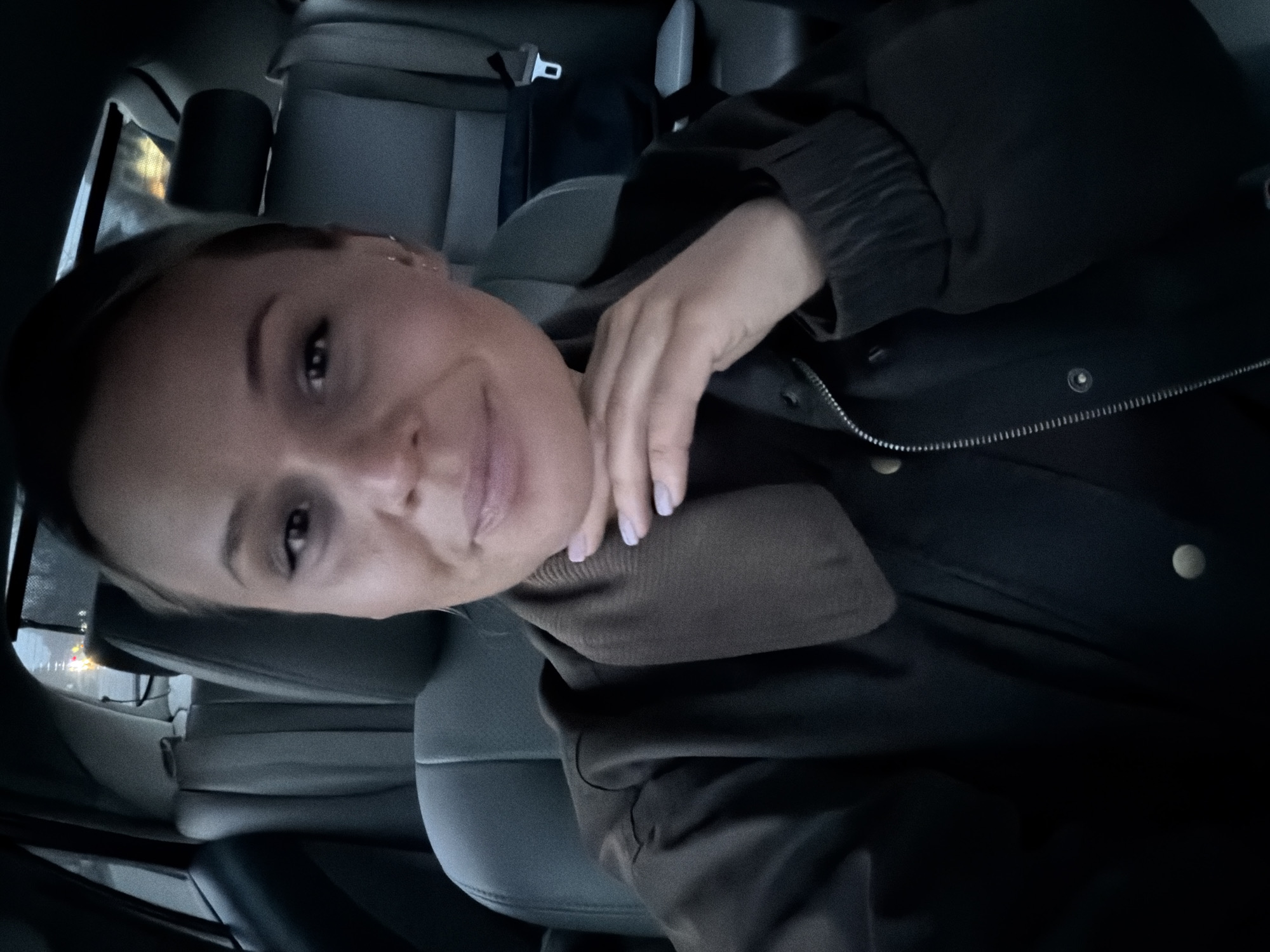 The image shows a woman seated in the passenger seat of a car. The background suggests the interior of the vehicle, including the seats and other car elements. The woman is wearing a dark coat and appears to be posing for a selfie or photo. The specific location within Sarapul, Russia, is not identifiable from the visual information. There are no visible actions, interactions, or specific environmental details beyond the car interior.