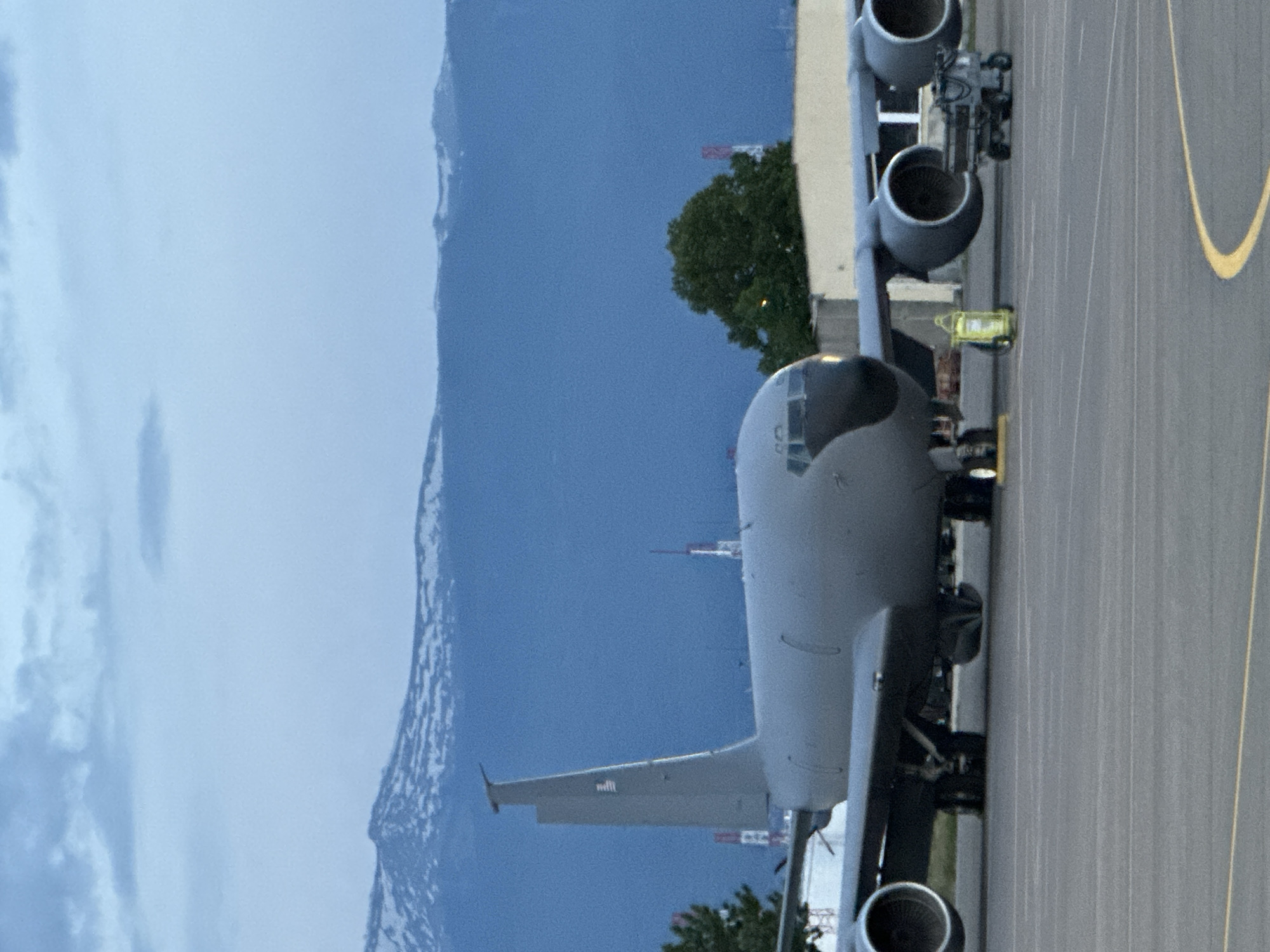 An aerial view shows a United States Air Force Boeing KC-135 Stratotanker aircraft parked on an airport tarmac, likely for refueling operations. The KC-135 has four turbofan engines under its wings. A mountain range with snow is in the background under a hazy sky. The location cannot be positively determined to be Sofia, Bulgaria without additional evidence, however, the scene resembles an airport adjacent to a mountain range.