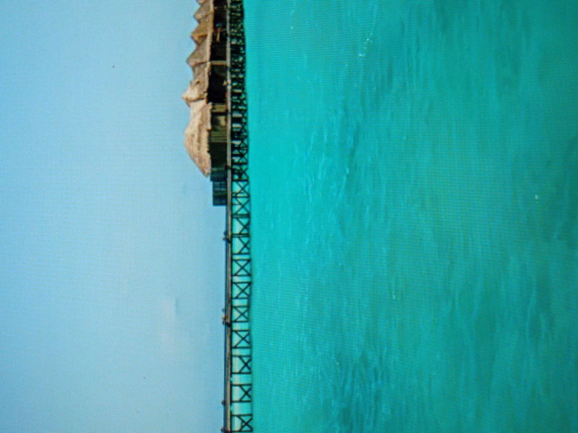 The image depicts overwater bungalows with thatched roofs on a pier extending into turquoise water. The sky is a clear, pale blue. There are no people or animals visible in the image. The scene is serene and appears to be a resort or vacation destination. The city of Mukachevo, Ukraine is not depicted in this image.