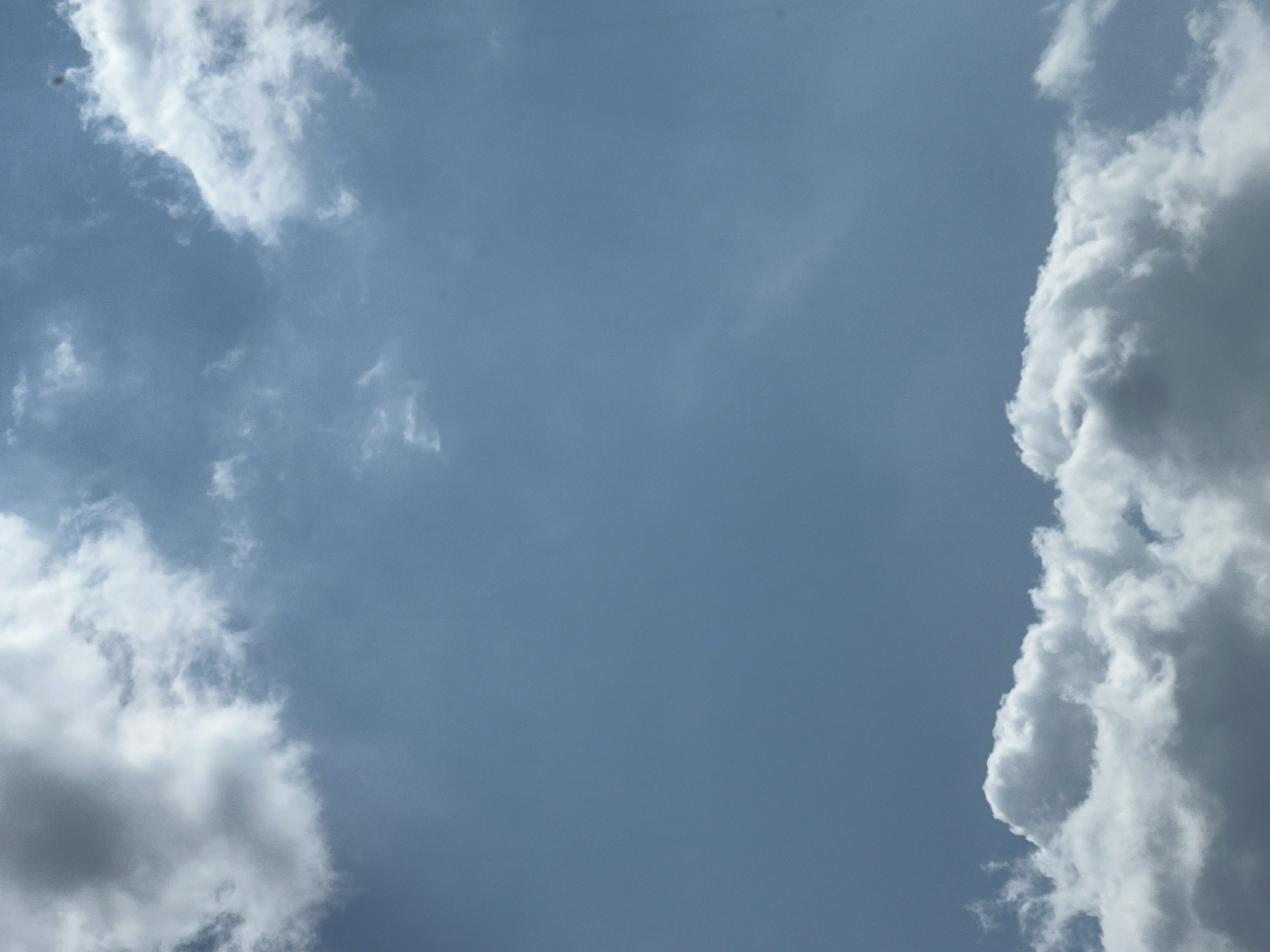 This image depicts a cloudy sky with a band of clouds along the bottom and scattered clouds towards the top. The sky is a muted blue. There is no identifiable location in Warsaw, Poland, visible in this image. The scene is entirely natural and does not contain any people, subjects, objects, or actions.