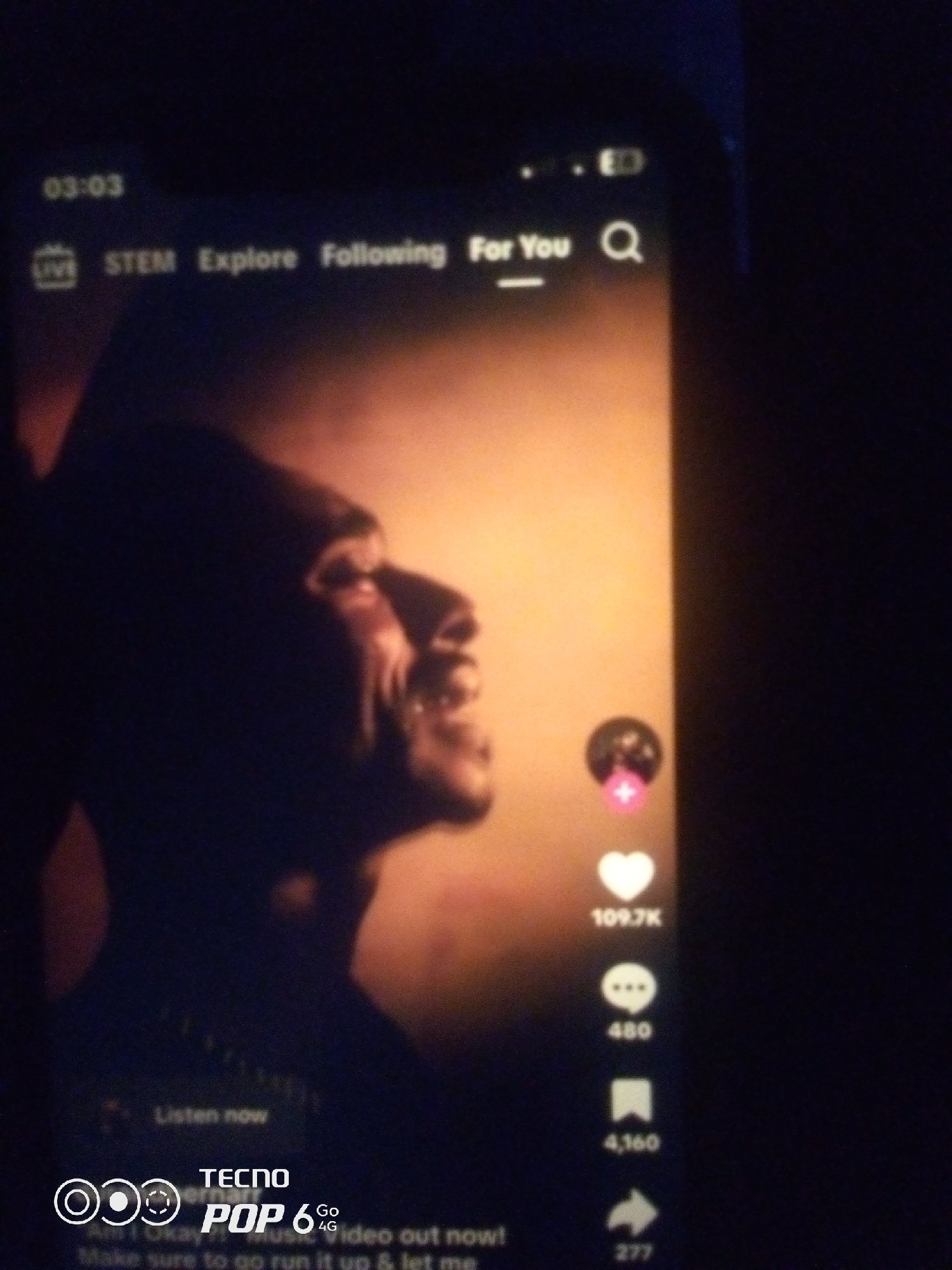 The image shows a close-up of a smartphone screen displaying a video. The video features a man's profile in silhouette against a warm, orange-toned background with beams of light. On the right side of the screen, there are social media engagement icons: a heart with "109.7K" below it, a speech bubble with "480" below it, and a bookmark icon with "4,160" below it, and a share icon with "277" below it. At the bottom of the screen, a logo for "TECNO POP 6 Go 4G" is visible, along with text that appears to be song lyrics: "Ah, I okay! My music video out now! Make sure to go run it up & let me." The top of the screen shows time "03:03" and navigation options for "LIVE", "STEM", "Explore", "Following", and "For You", along with a search icon. There is no discernible information in the image that indicates the location as Howayi, Nigeria.