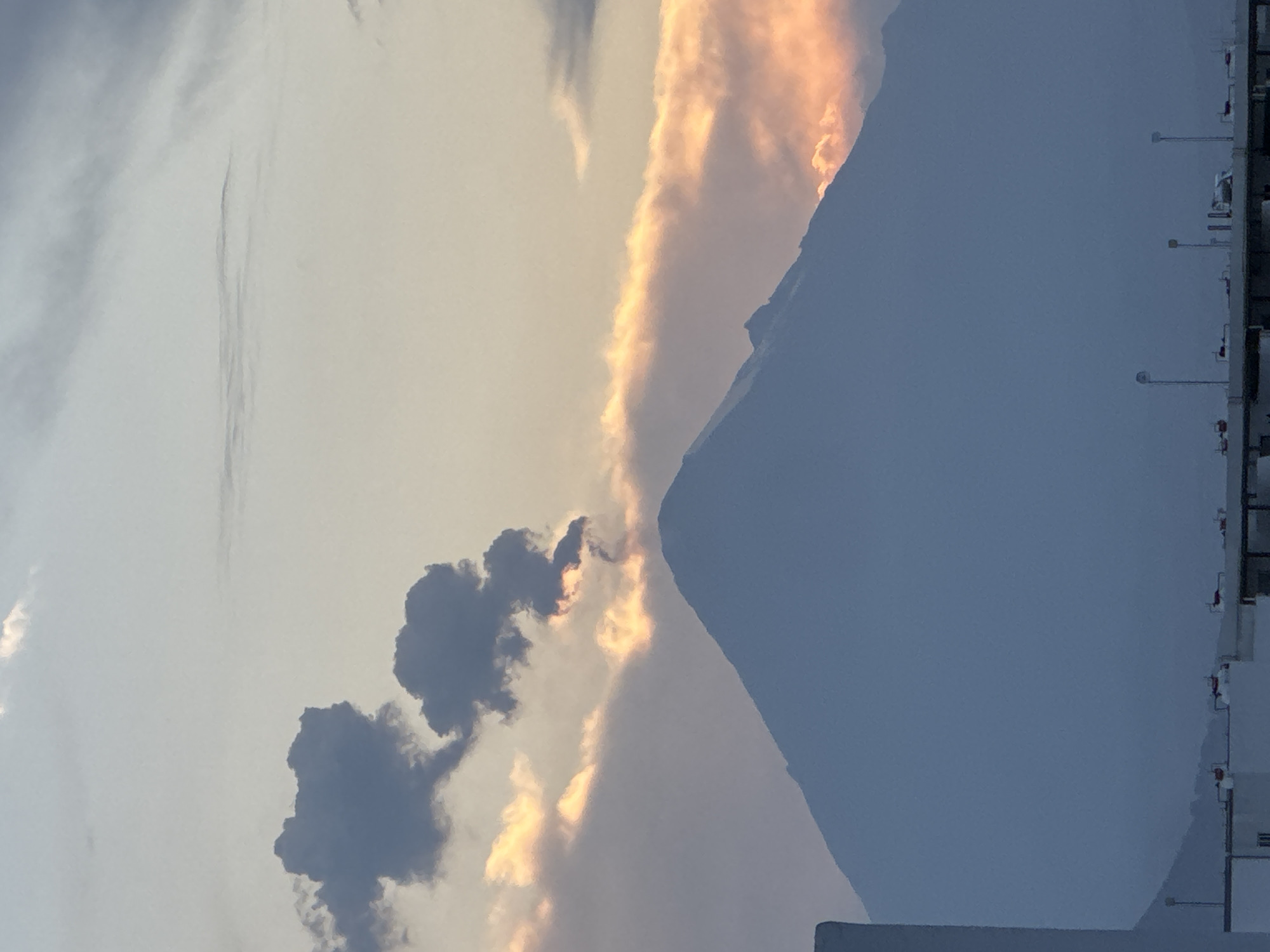 The image shows a dusky sky above what appears to be the edge of a mountain and a building. On the left, dark clouds are visible against a lighter sky with hints of orange light. To the right, a large, dark mountain silhouette dominates a significant portion of the frame. A building structure is visible in the lower right corner. Based on the instructions, the location is the city of San Francisco Ocotlán (Ocotlán), Mexico.