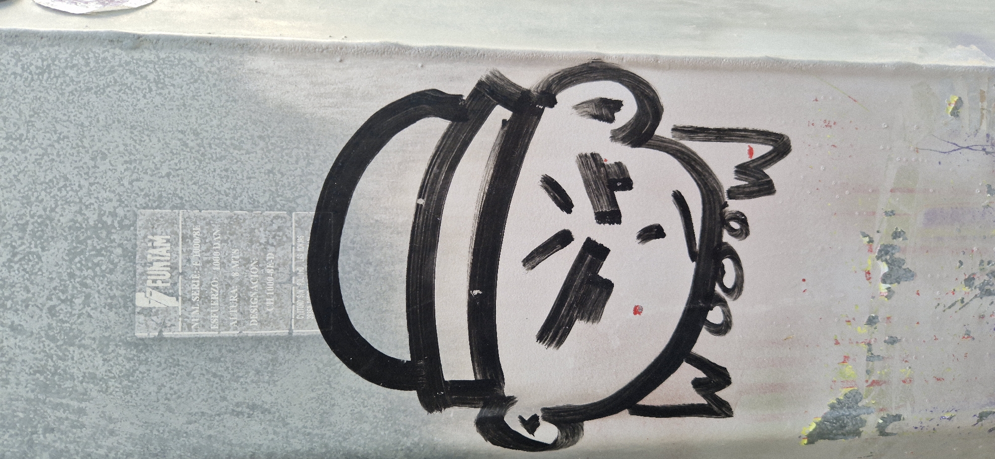 A close-up, eye-level shot captures a piece of street art on a textured, light gray metal surface. The artwork is a black ink drawing of a stylized cartoon head with a flat top and large ears. The head has angry, slanted eyes, a small nose, and a closed mouth with a red dot above it. Below the mouth, the word "WOOOOW" is written in black ink, with small red dots placed on the letters "O" and "W". A faded label with text is visible above the drawing, featuring the word "FUNTAM" at the top. The background is a mottled light gray with some peeling paint and colorful splatters at the bottom. The lighting is even, with no distinct shadows.