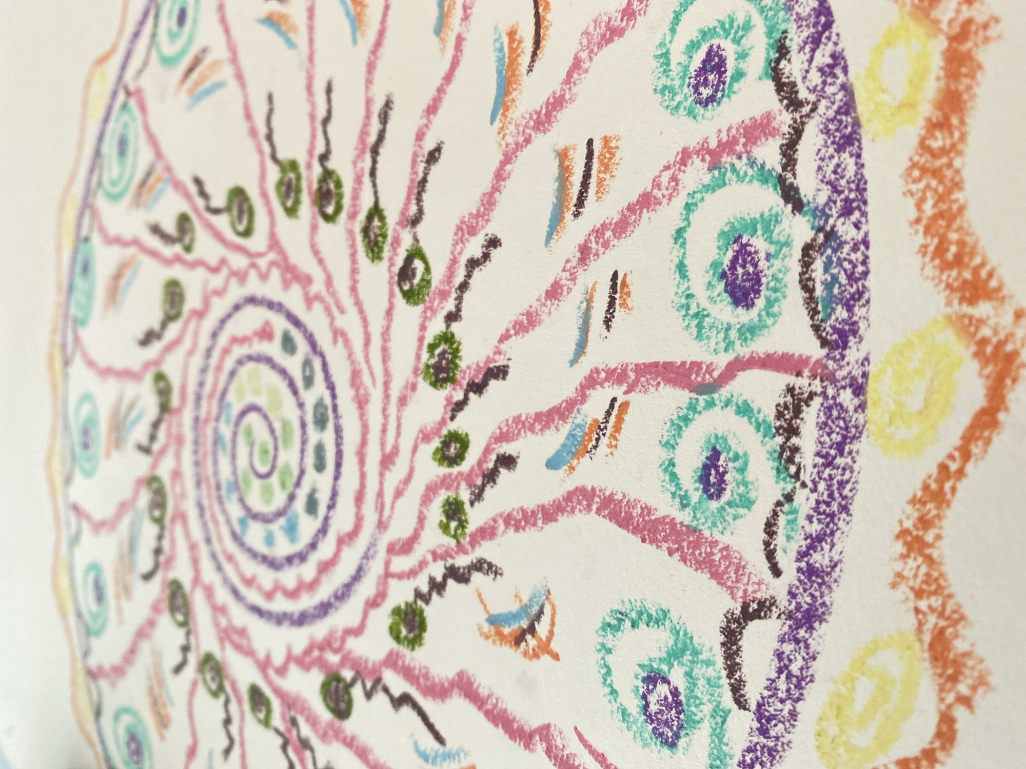 The image shows a close-up of a drawing, likely created with crayons or oil pastels. The drawing features a spiral pattern in the center, expanding outwards. The colors used include green, purple, blue, pink, brown, orange, and yellow. The drawing appears to be on white paper. No specific location in Yekaterinburg, Russia, is apparent.