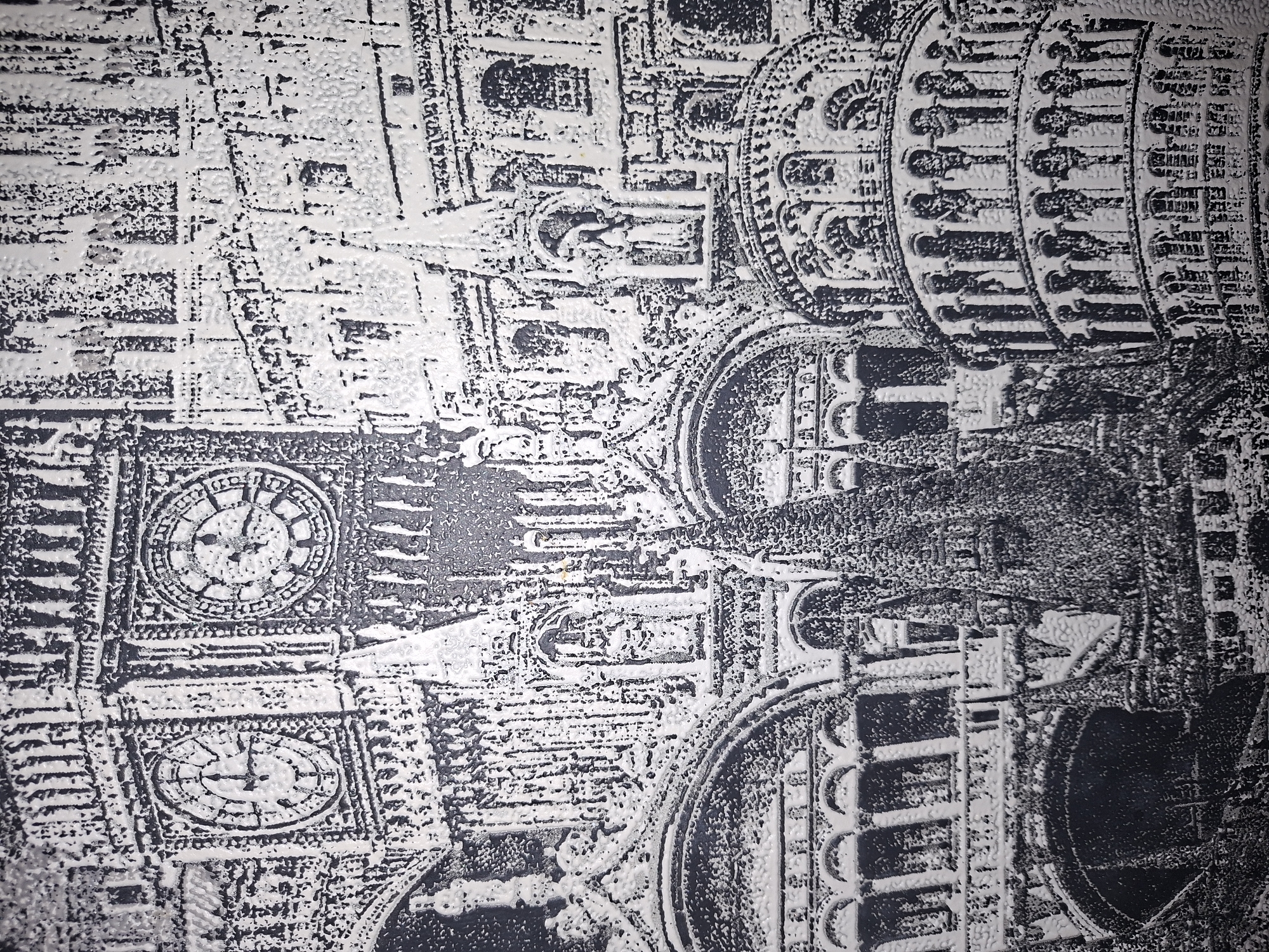 The image is a black and white, textured, close-up photographic depiction of a collage of famous architectural landmarks. On the left, the clock face of Big Ben is visible, with Roman numerals and clock hands indicating a time close to 5:35. To the right of Big Ben, the intricate stonework of other Gothic-style buildings is rendered in high detail, featuring arched windows, columns, and statues. In the lower right portion of the image, the Leaning Tower of Pisa is depicted, its curved structure and arcaded levels clearly discernible. The overall texture suggests it might be a print on a textured surface or a bas-relief carving. The collage combines elements of London and Pisa, creating a composite urban landscape. There are no people, animals, or specific environmental details of Nikolaevka, Russia, present in this image.