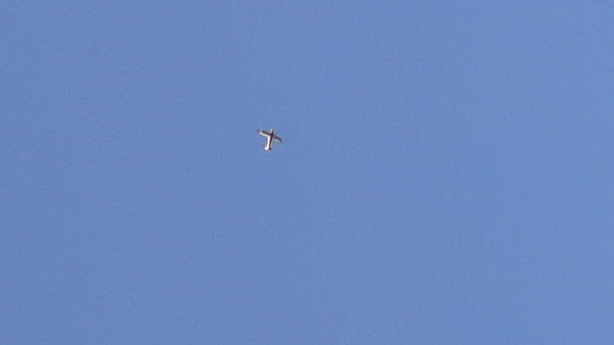 A single, small, white airplane is captured in mid-flight against a clear blue sky. The airplane is positioned slightly to the right of the center of the frame and appears to be a propeller-driven aircraft. No people or other objects are visible in the image. The environment is a vast expanse of unblemished sky. The image does not provide any specific details that would allow for the determination of its location within the city of Vadul lui Voda, Moldova.