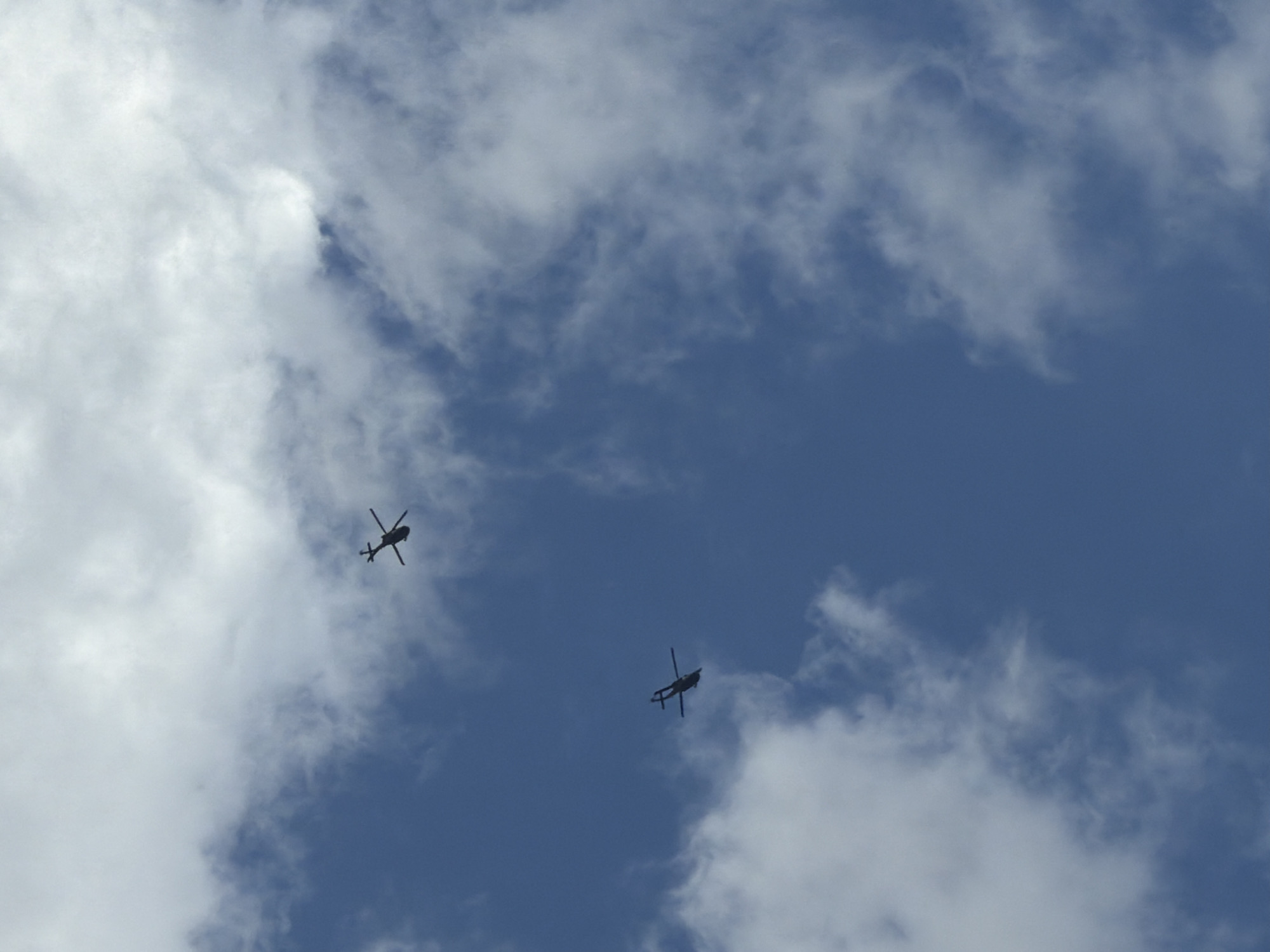 Two helicopters are visible in the sky, silhouetted against a blue sky with scattered clouds. The helicopters appear to be military or civilian aircraft, with a distinct rotor system. The lower helicopter is closer to the camera, while the upper helicopter is further away and slightly to the right. The image does not provide any specific details about the location within the city of Zlati Voyvoda, Bulgaria.