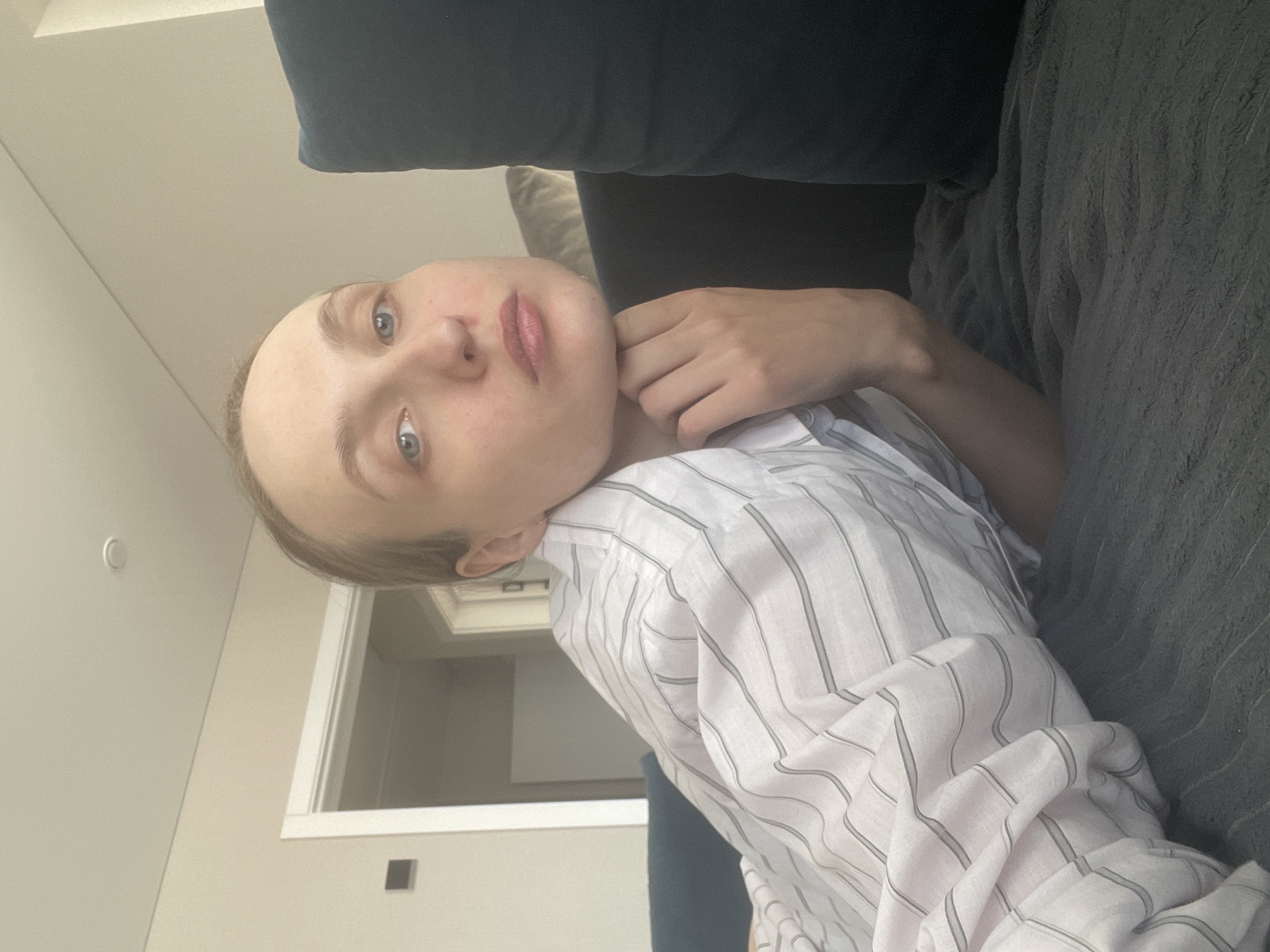 A person is reclining on a couch. The person is wearing a striped shirt and has their hand near their neck. The background includes a wall and a door frame. The location is not identifiable as Sepych, Russia from the image.
